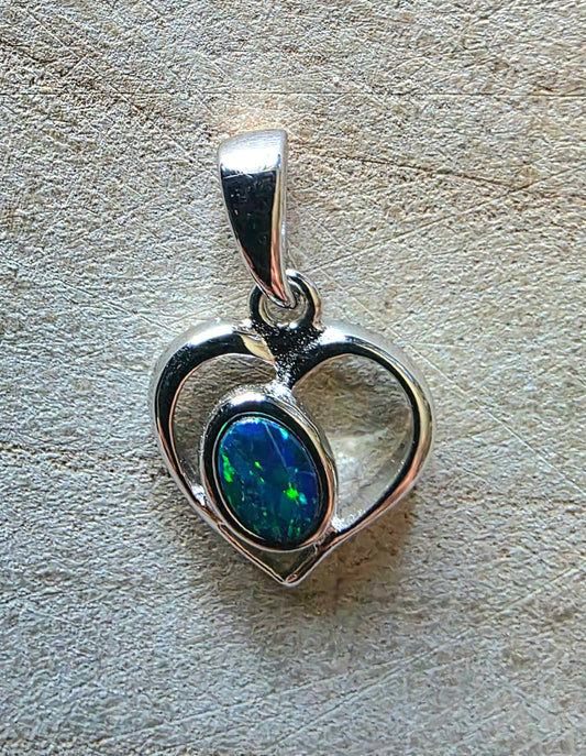 Silver heart-shaped pendant with a blue opal on a textured surface