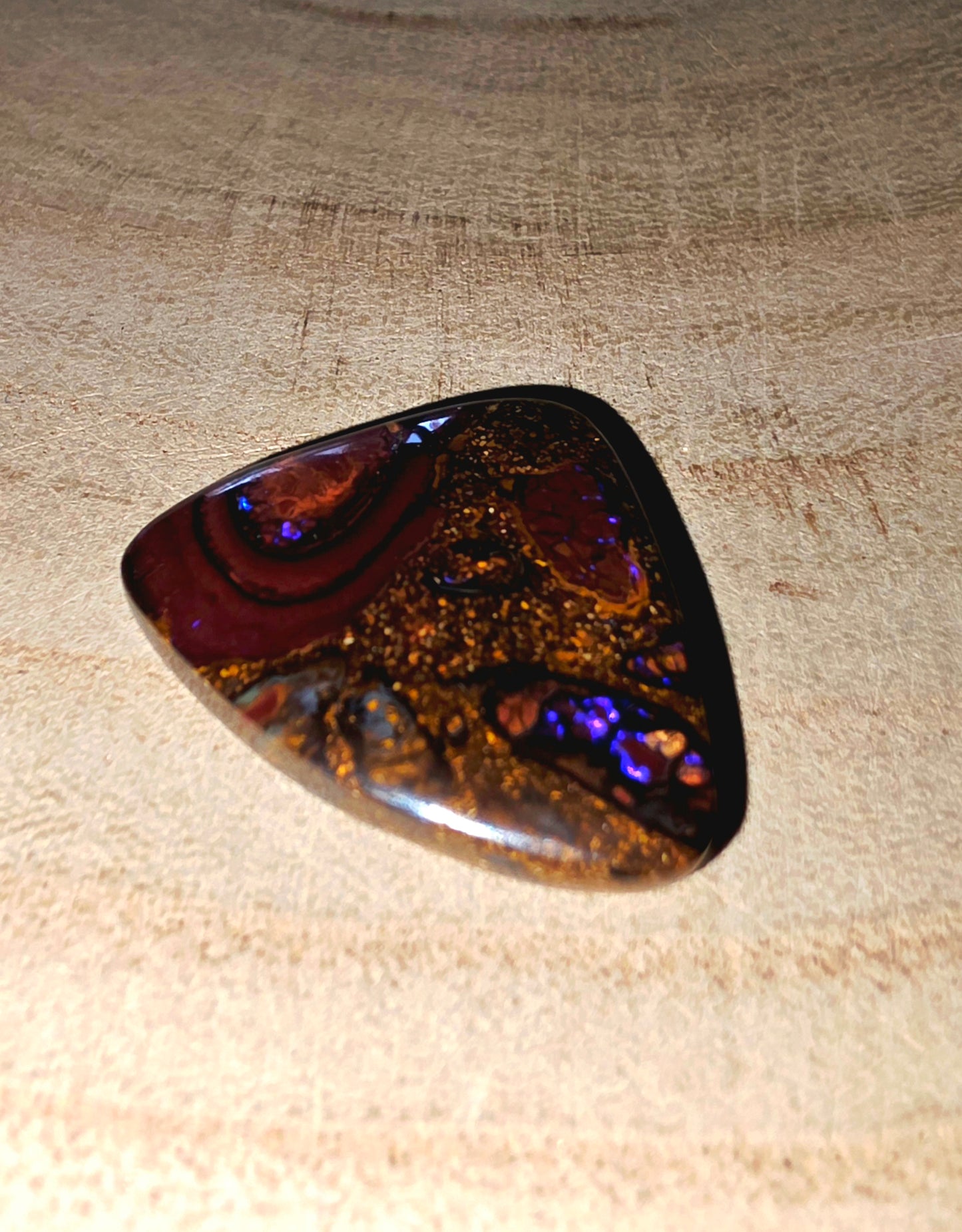 Polished boulder opal with multicoloured patterns on a textured fabric background