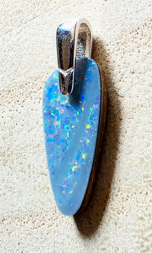 A blue opal pendant with a silver bail, resting on a textured beige surface.