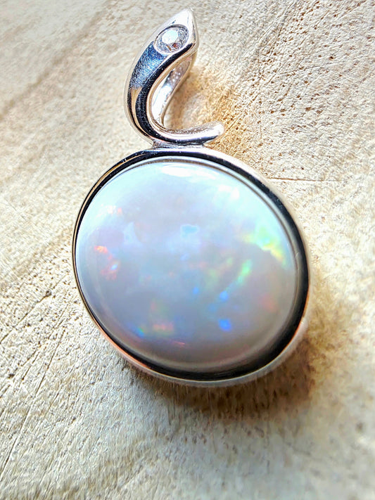 A silver pendant featuring a large, round cabochon opal gemstone with vibrant iridescent colours, set in a polished silver bezel with a curved bail.