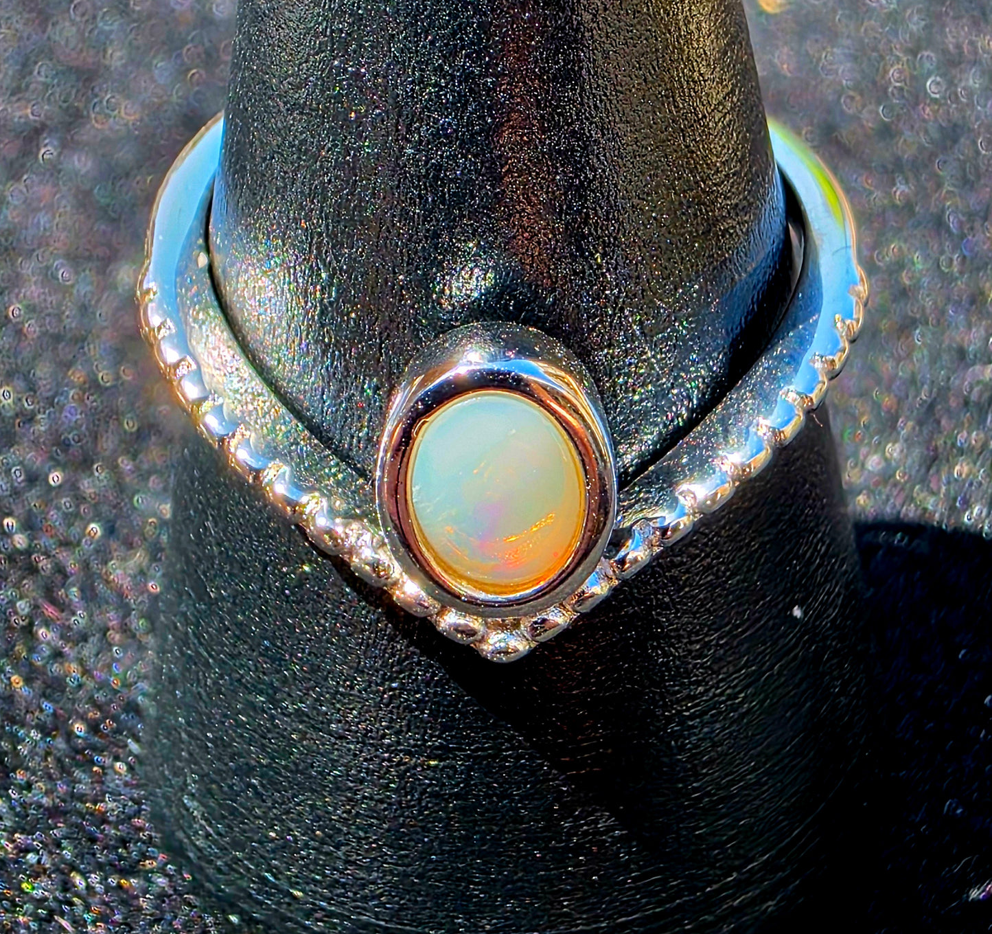 Ring with a silver band and central opal stone on a black stand.