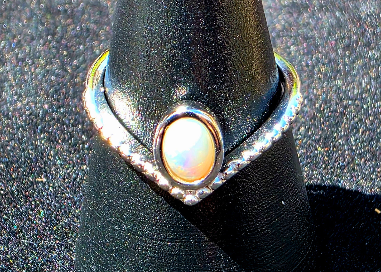 Silver ring with a central opal on a black stand