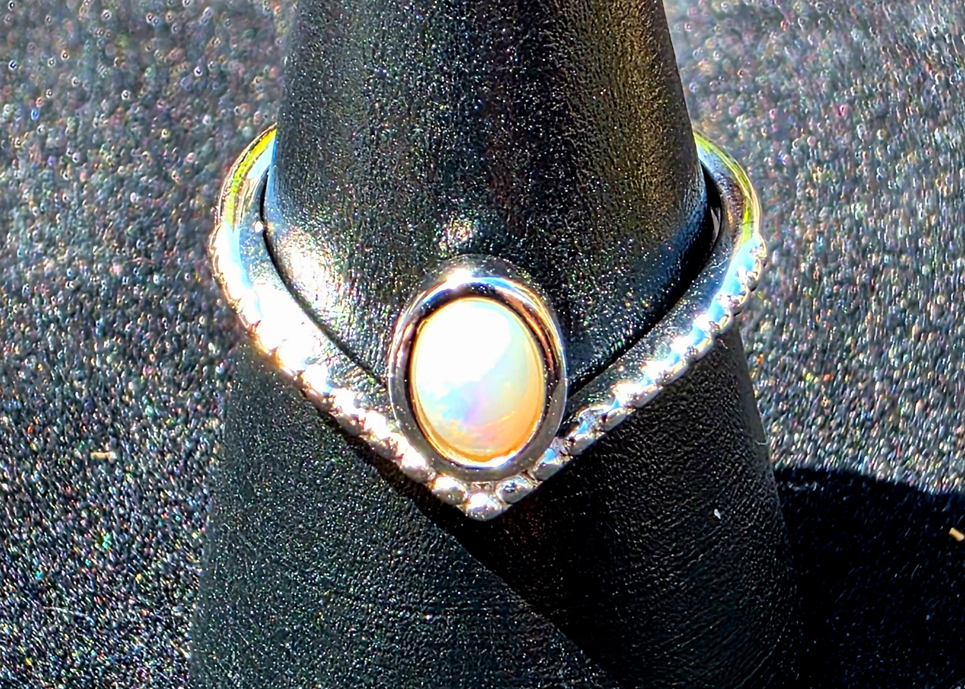 Silver ring with a central opal on a black stand