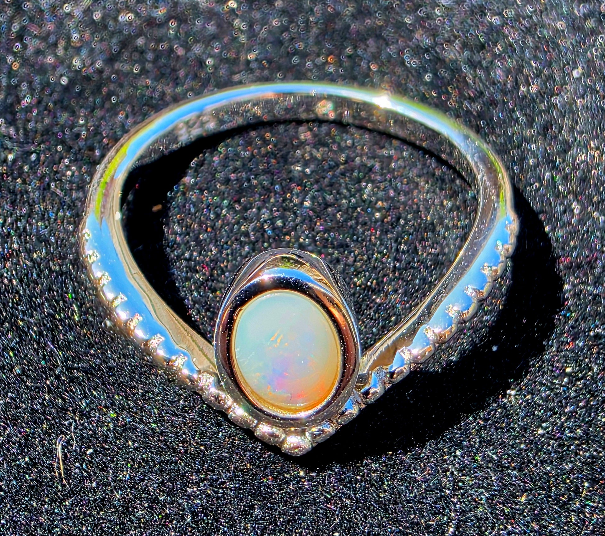 Silver ring with a central opal stone on a dark textured background