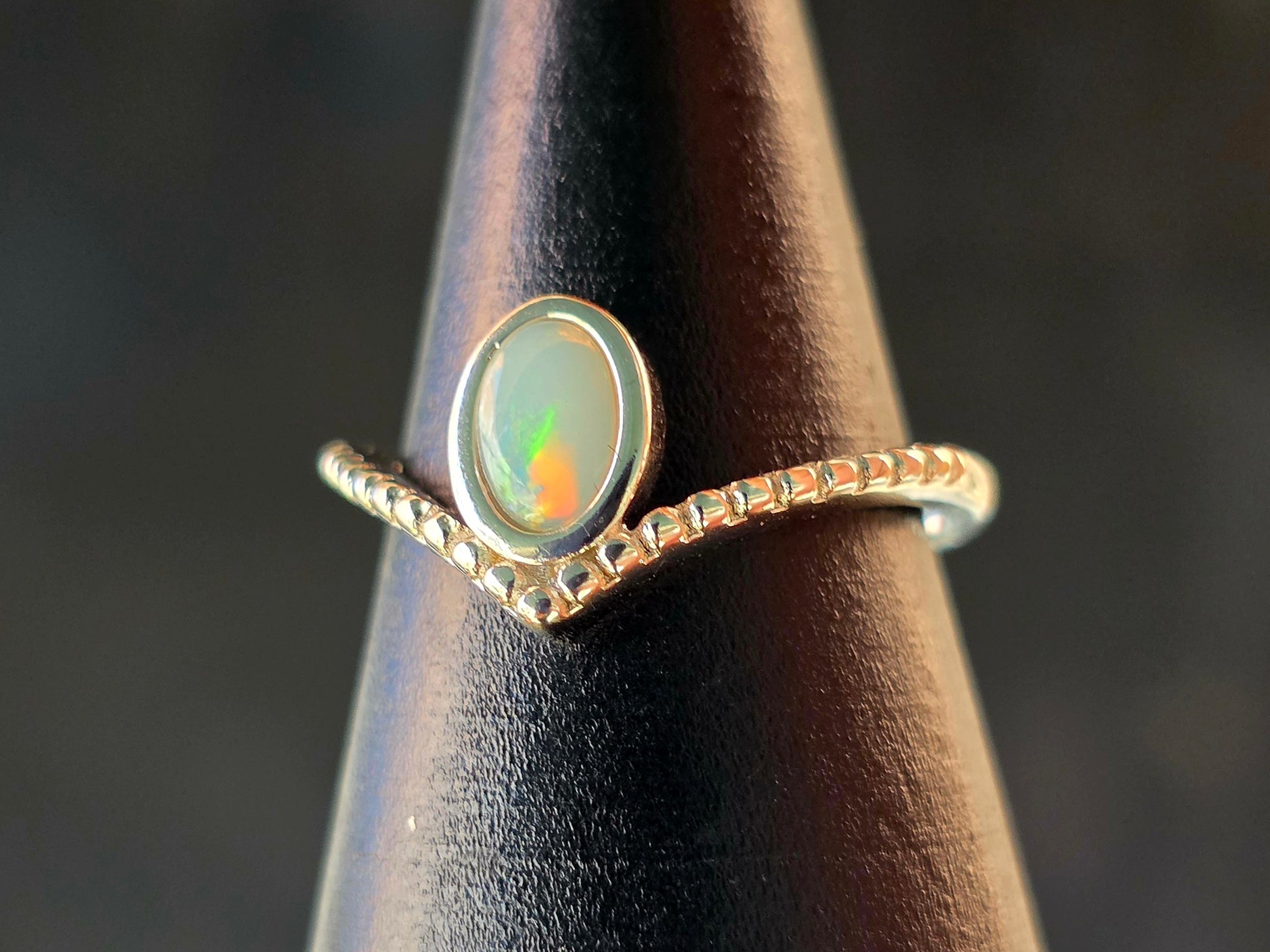 Silver ring with an opal stone on a dark brown stand