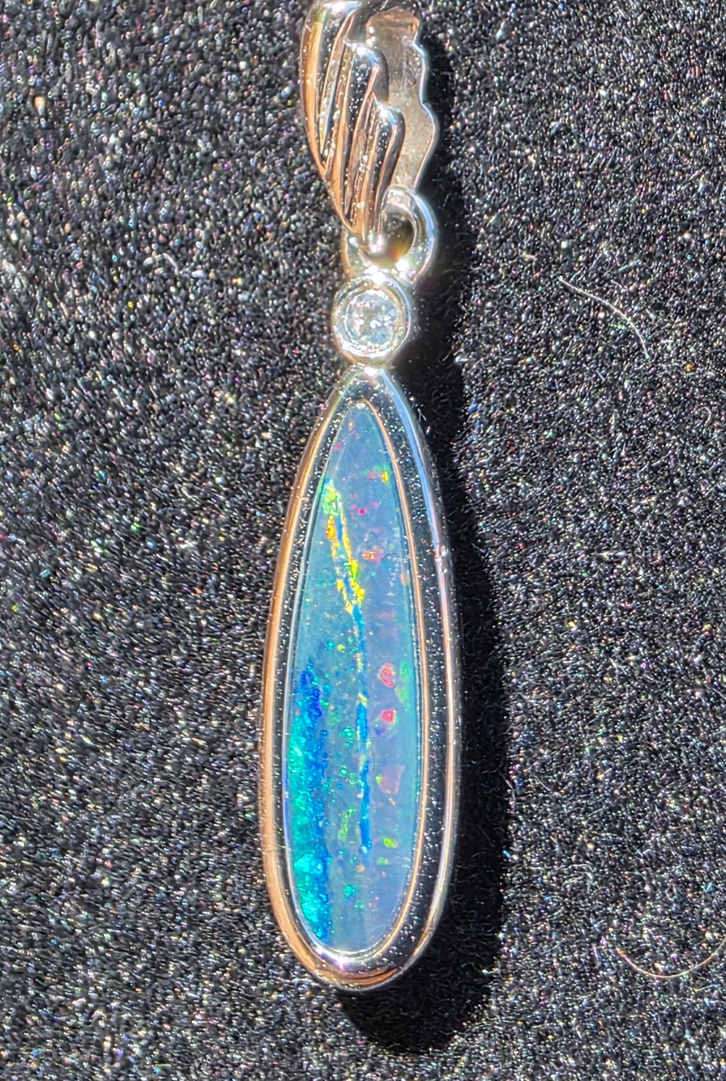 Teardrop-shaped opal pendant with silver setting on a dark textured background