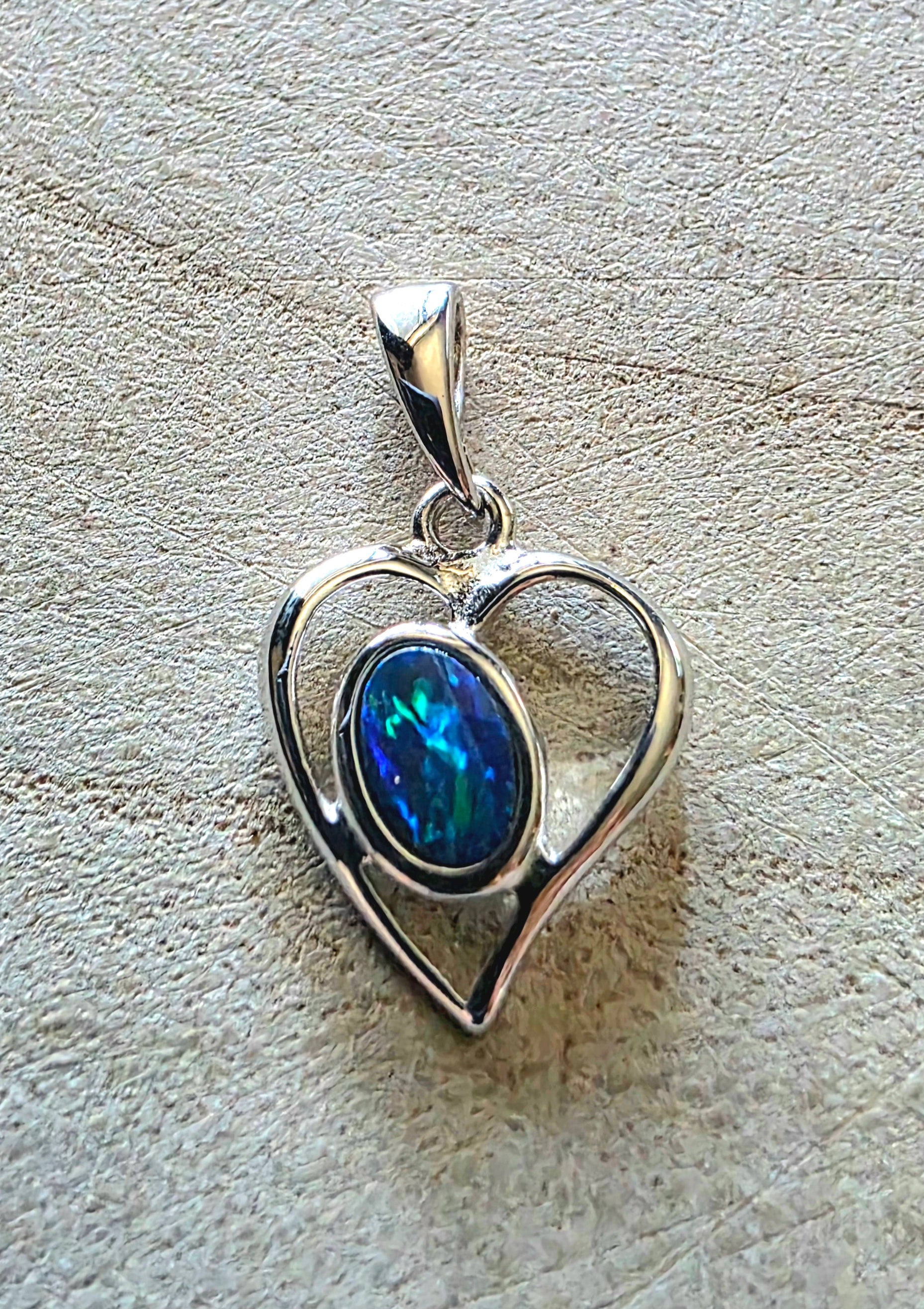 Silver heart-shaped pendant with a blue green opal on a textured surface