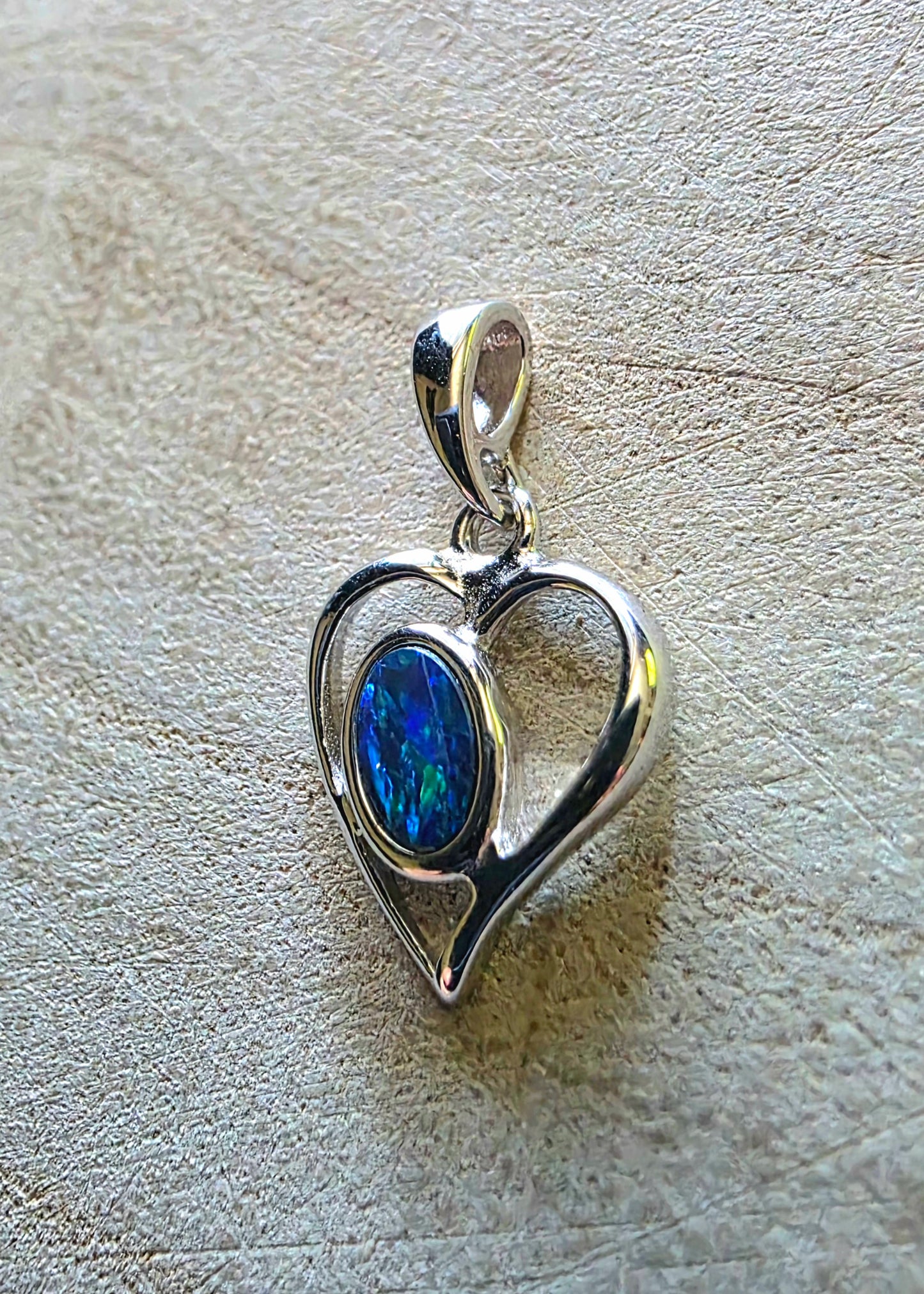 Silver heart-shaped pendant with a blue green opal on a textured beige surface