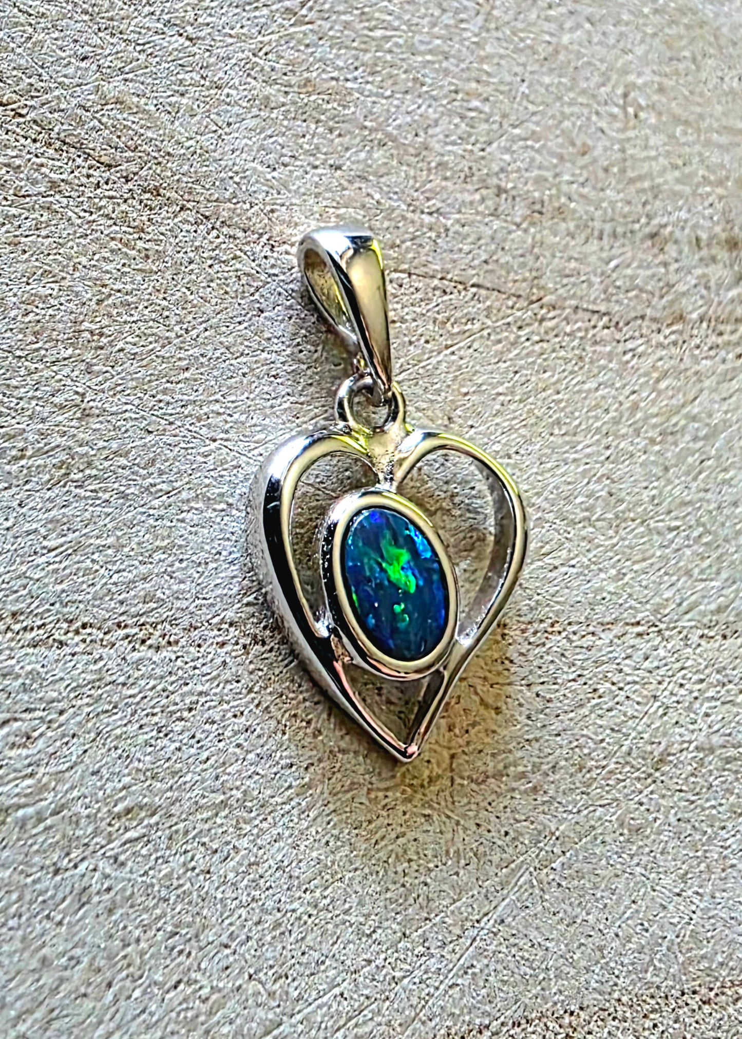 Heart-shaped pendant with a blue boulder opal on a textured beige background