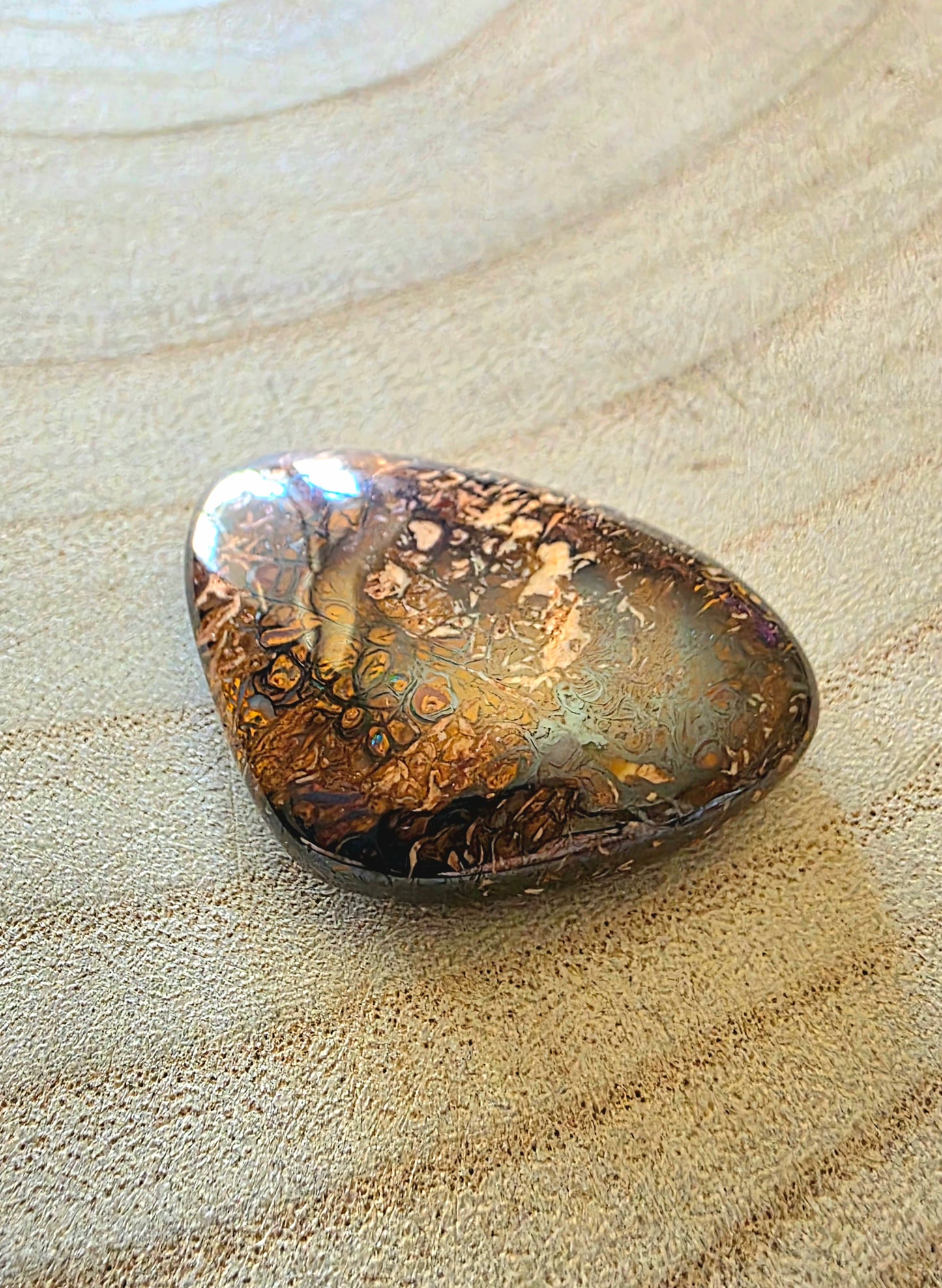 Polished boulder opal with marbled pattern on a textured beige surface