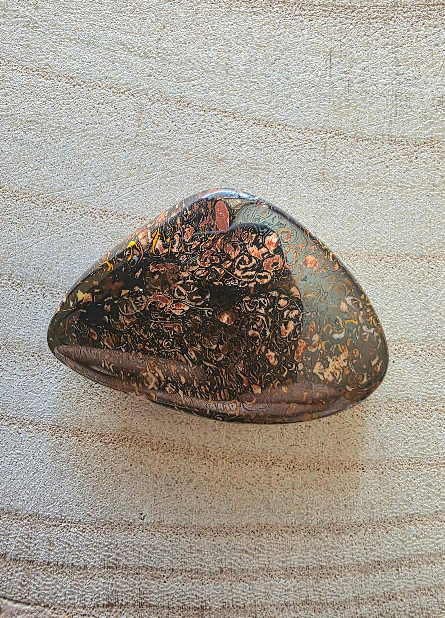 Polished boulder opal with marbled pattern on a textured beige surface