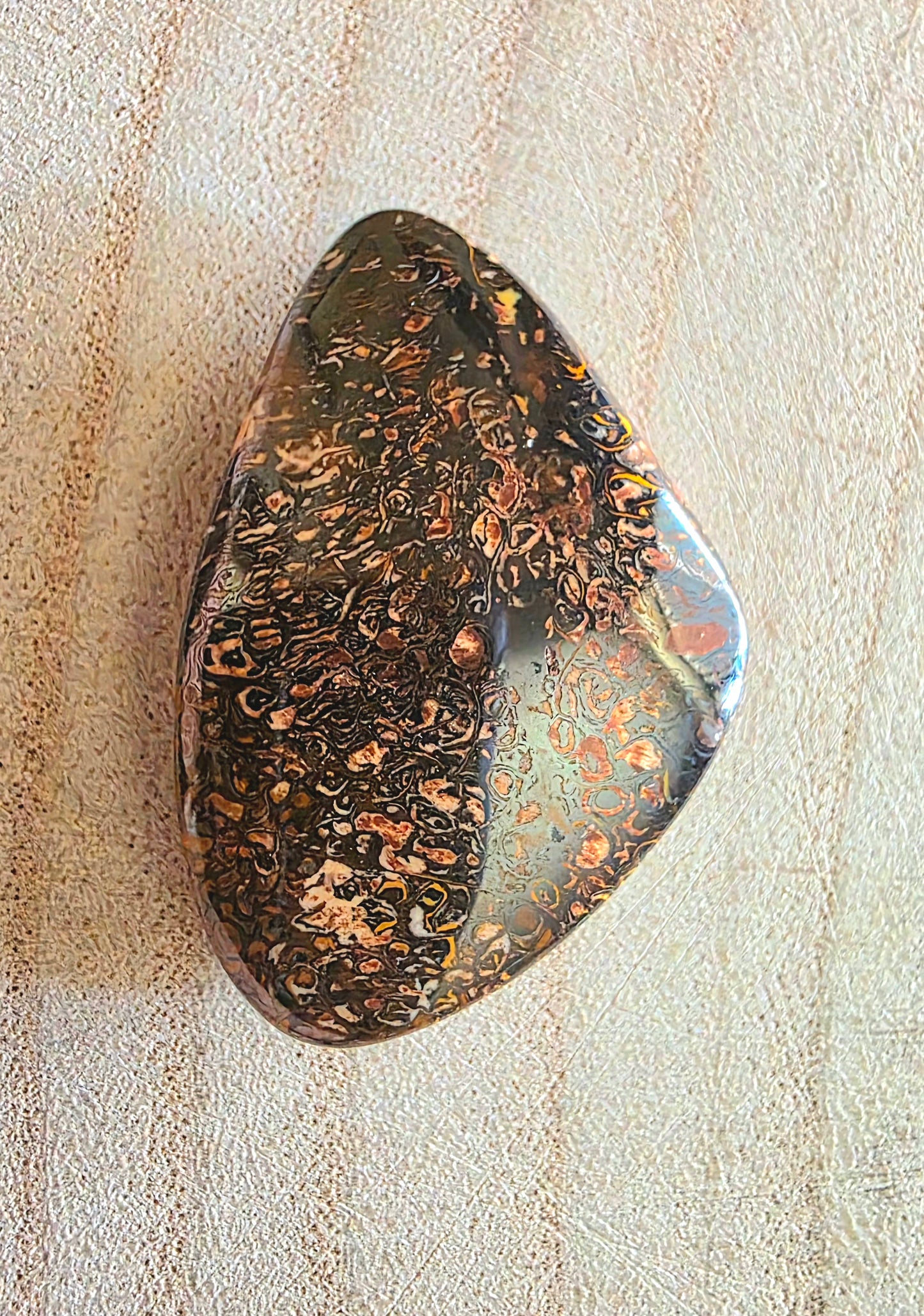 Polished boulder opal with marbled pattern on a textured beige surface