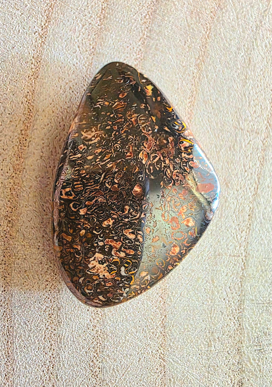 Polished boulder opal with marbled pattern on a textured beige surface