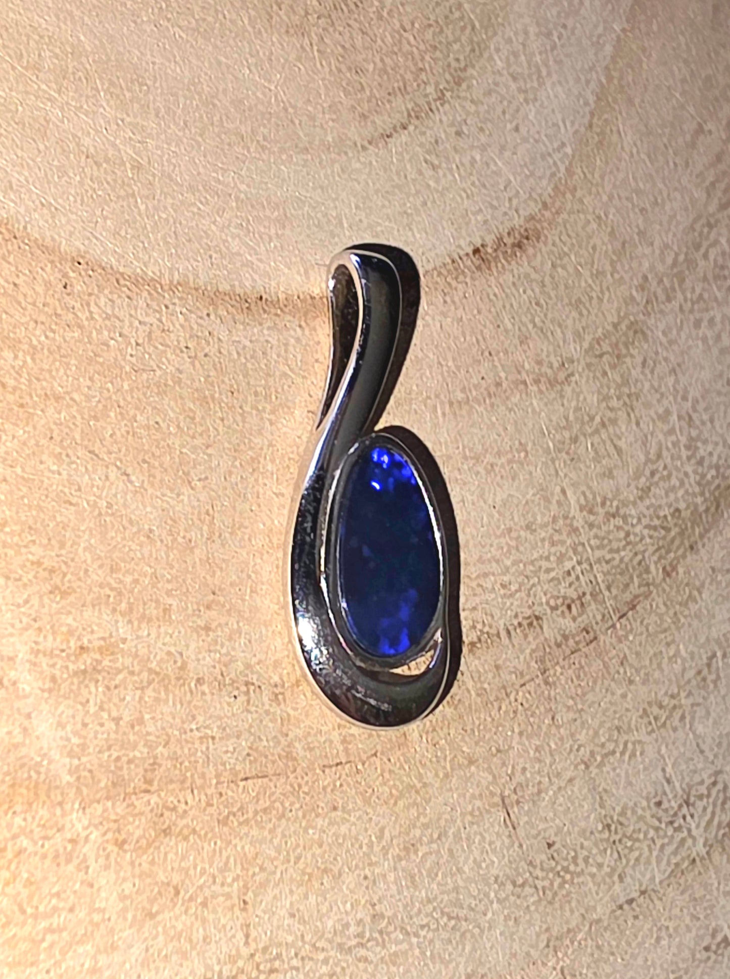 Silver pendant with a blue stone on a beige surface