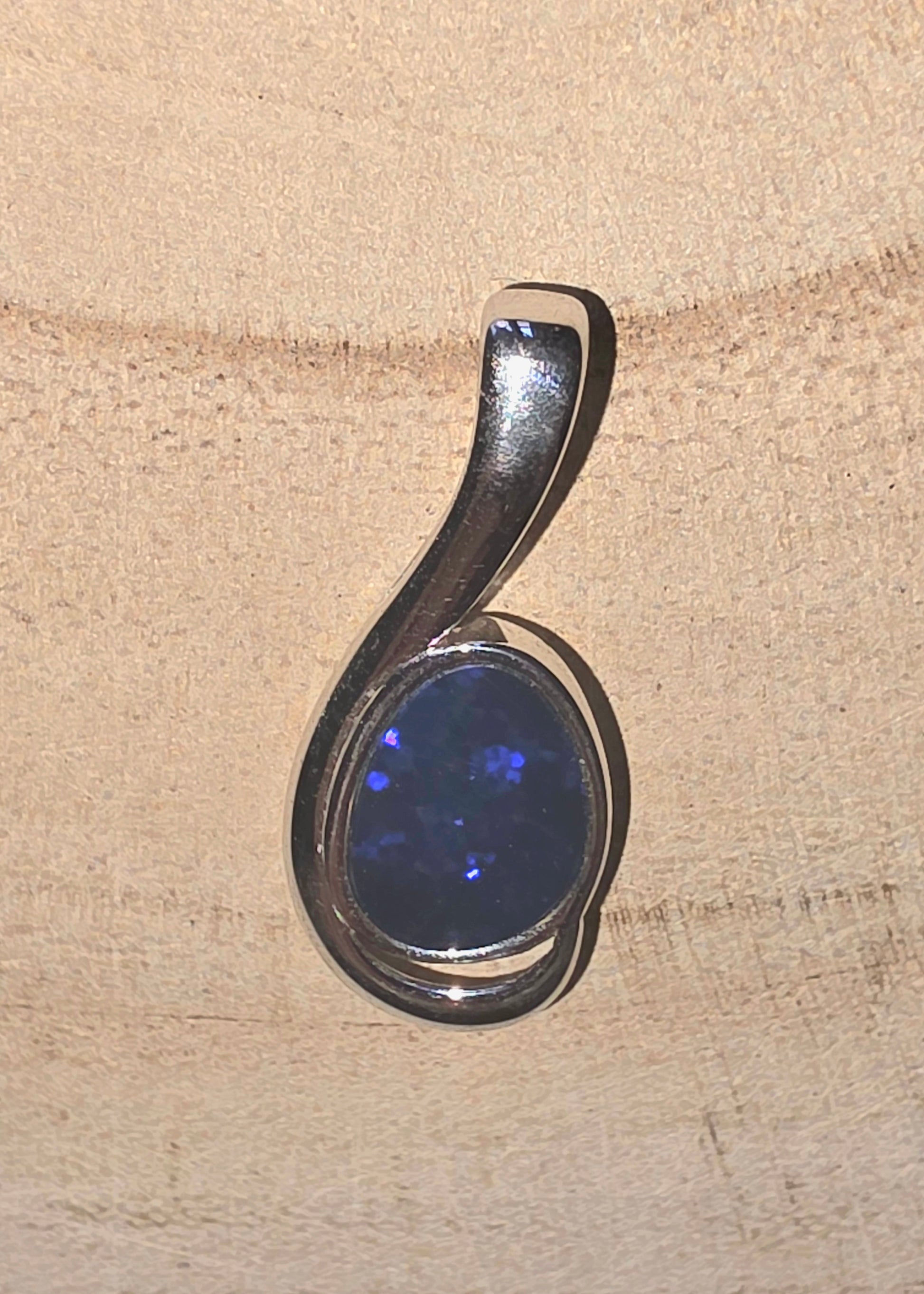 Silver pendant with a dark blue stone on a beige surface