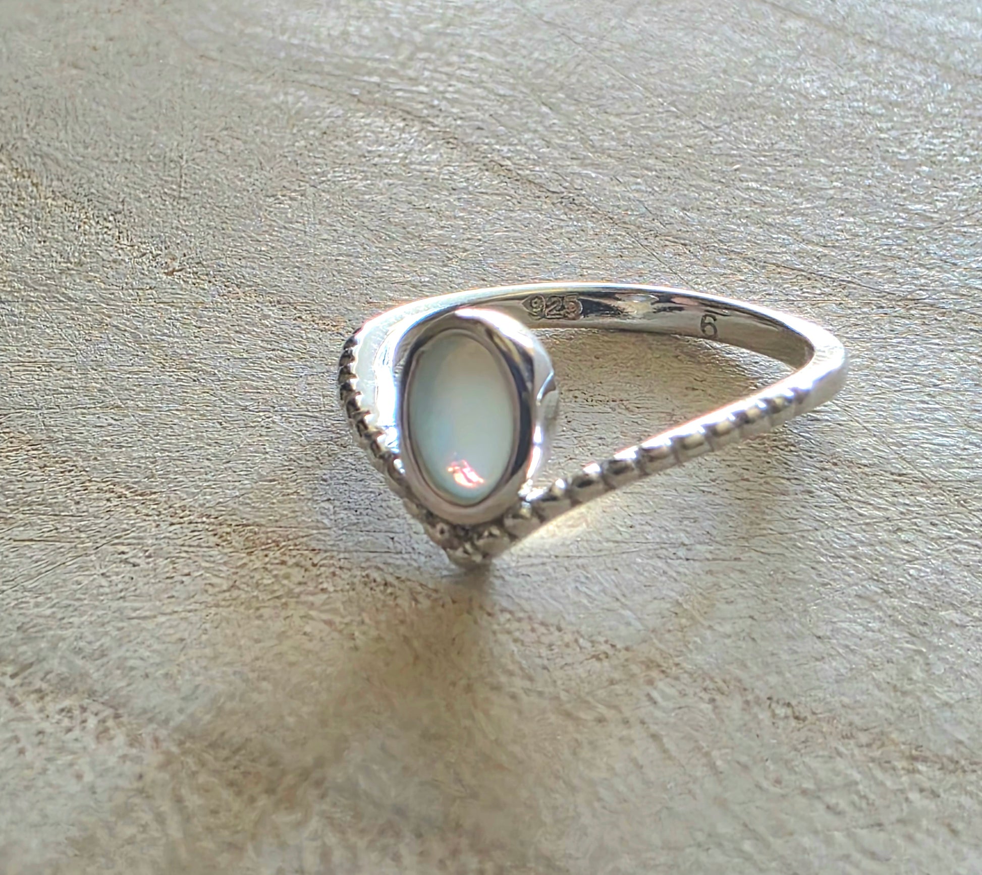 Silver ring with a light-coloured opal stone on a textured beige surface