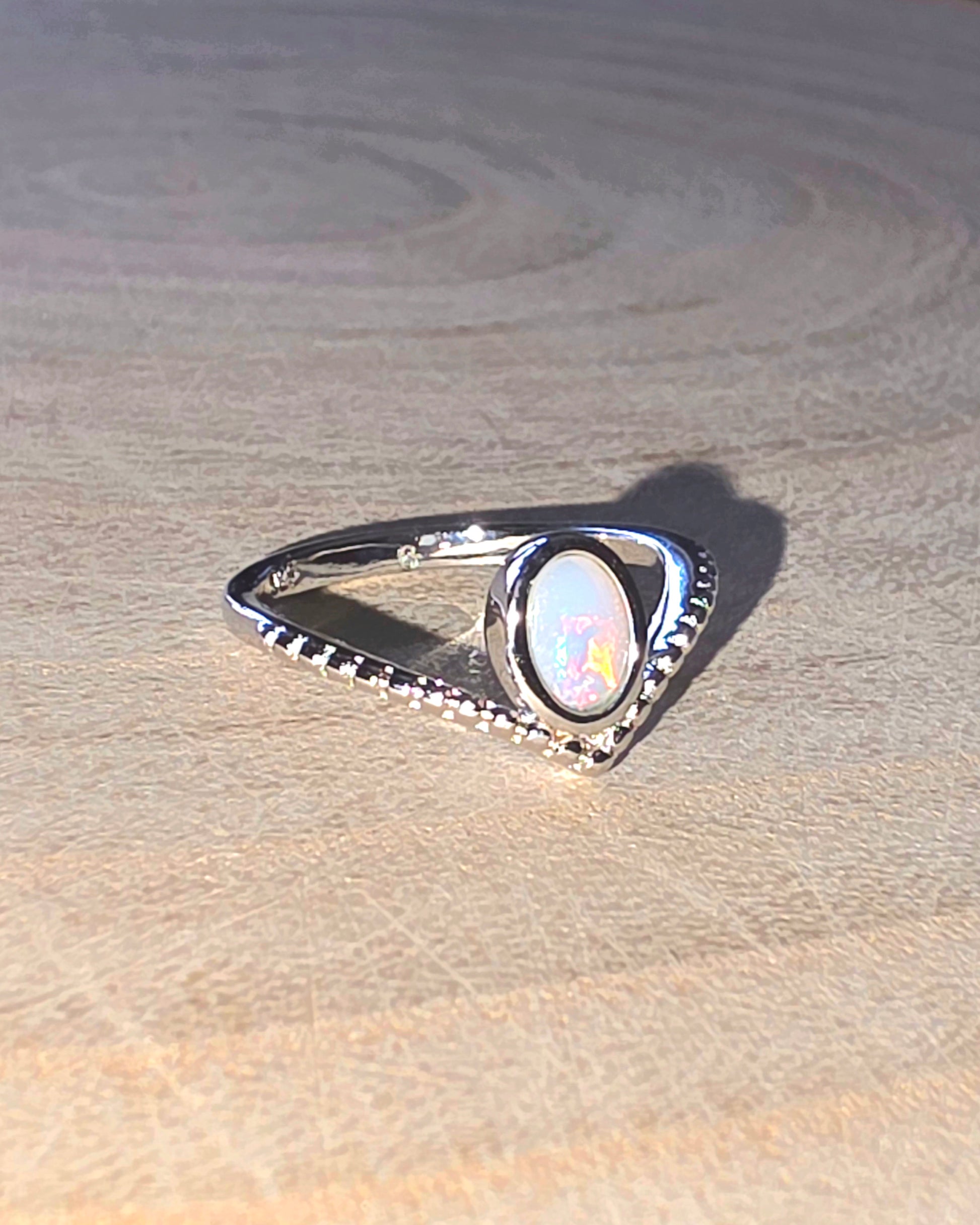 Silver ring with a central opal gemstone on a wooden surface