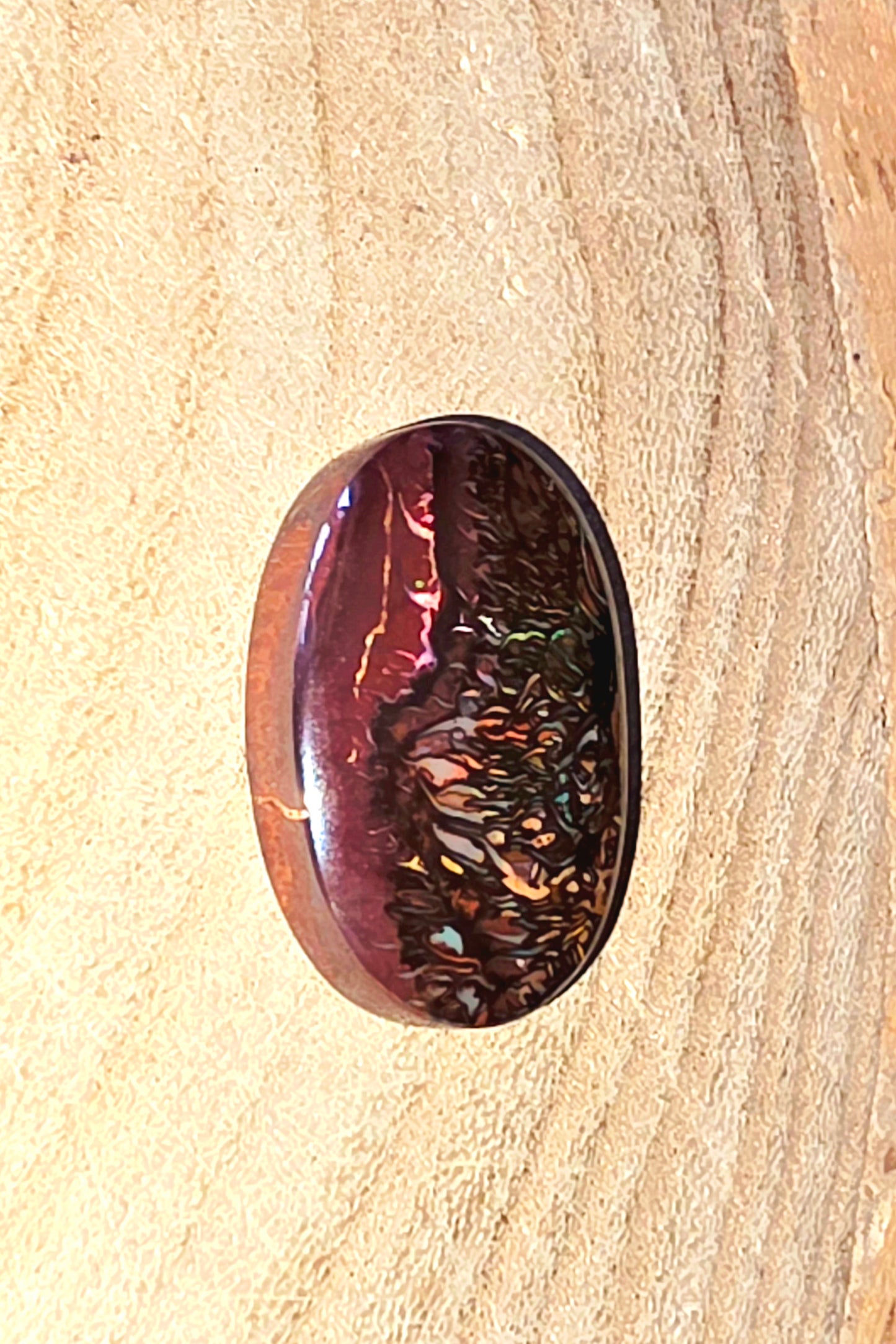 Oval-shaped gemstone with metallic sheen on a wooden surface