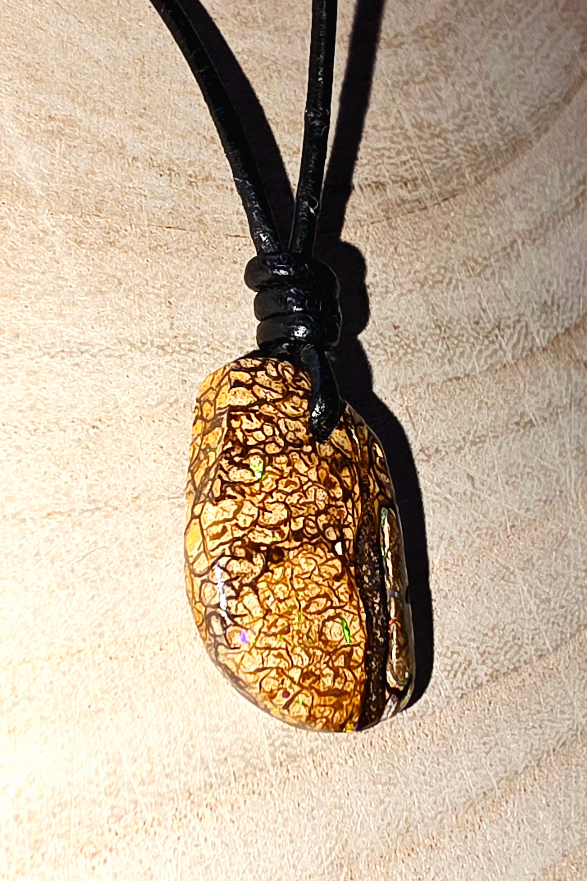 Opal pendant on a black cord against a beige background