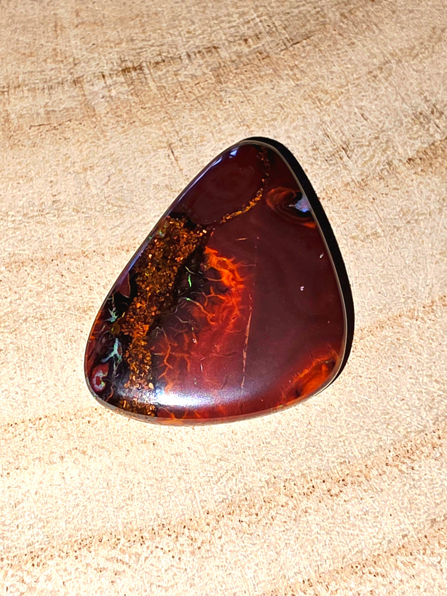 Polished brown and orange boulder opal on a beige textured background