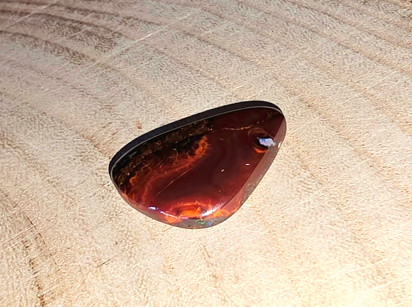 Polished brown and orange boulder opal on a beige textured background