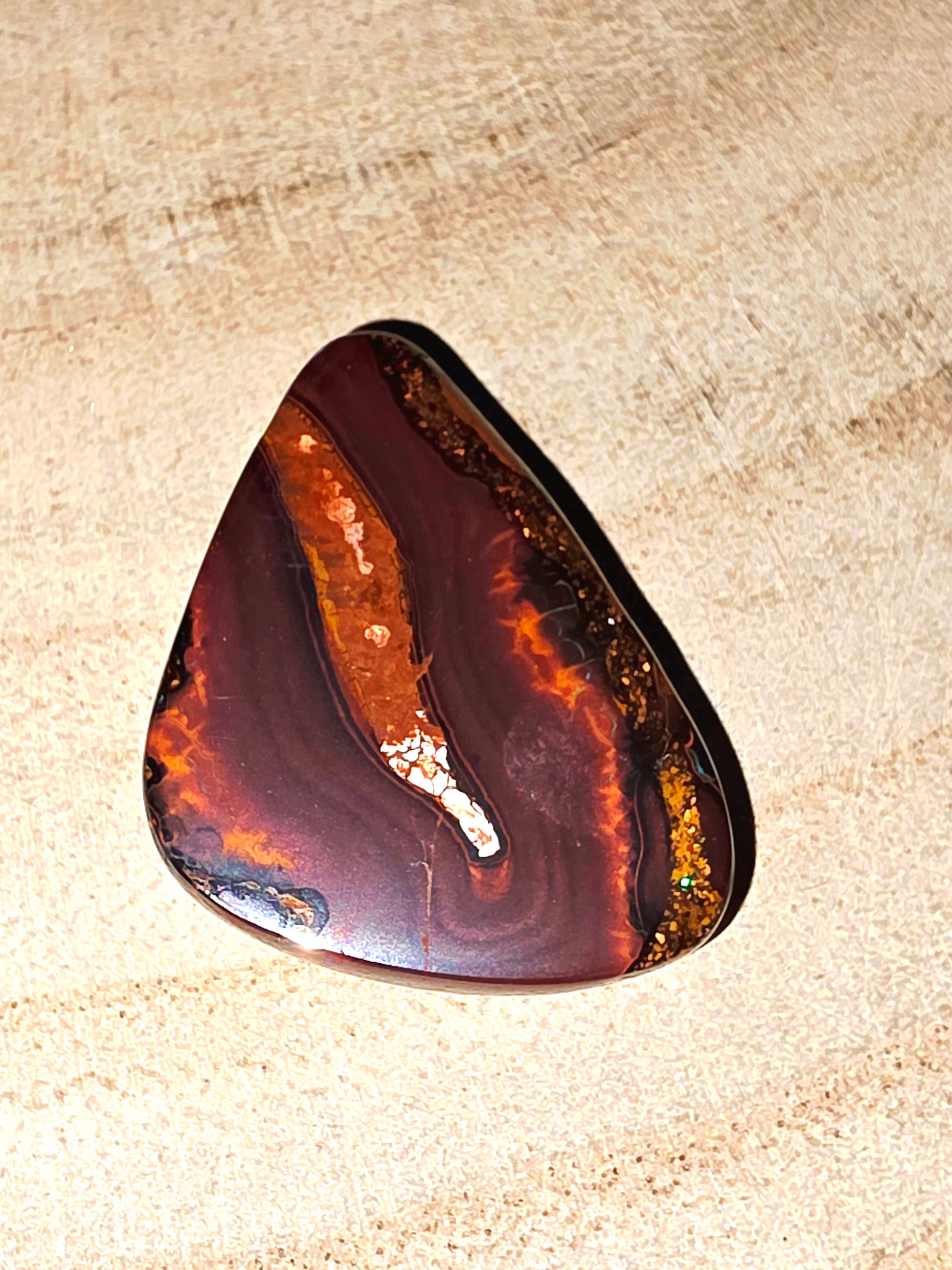 Polished boulder opal with brown and orange patterns on a beige surface