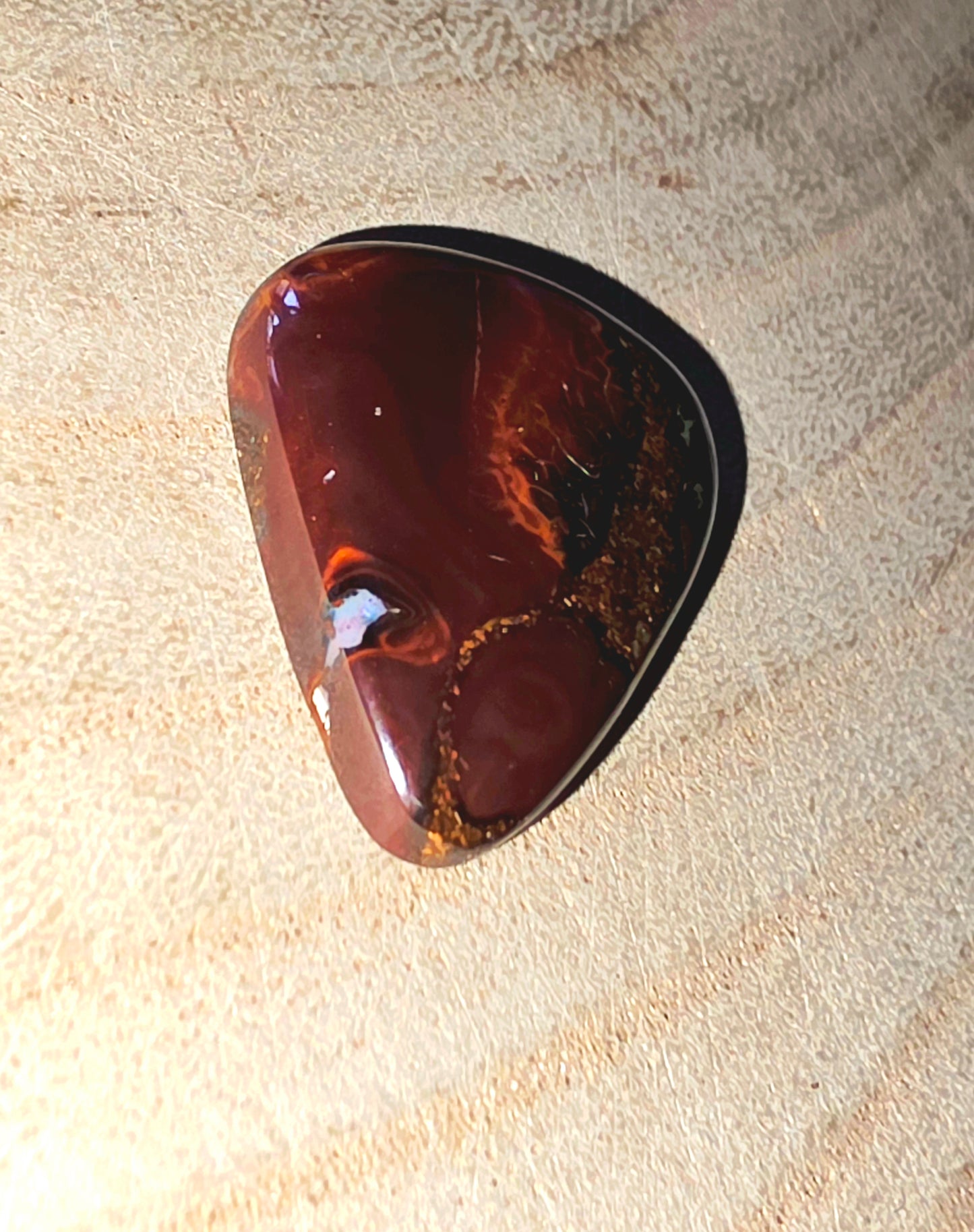 Polished brown opal stone on a textured beige surface