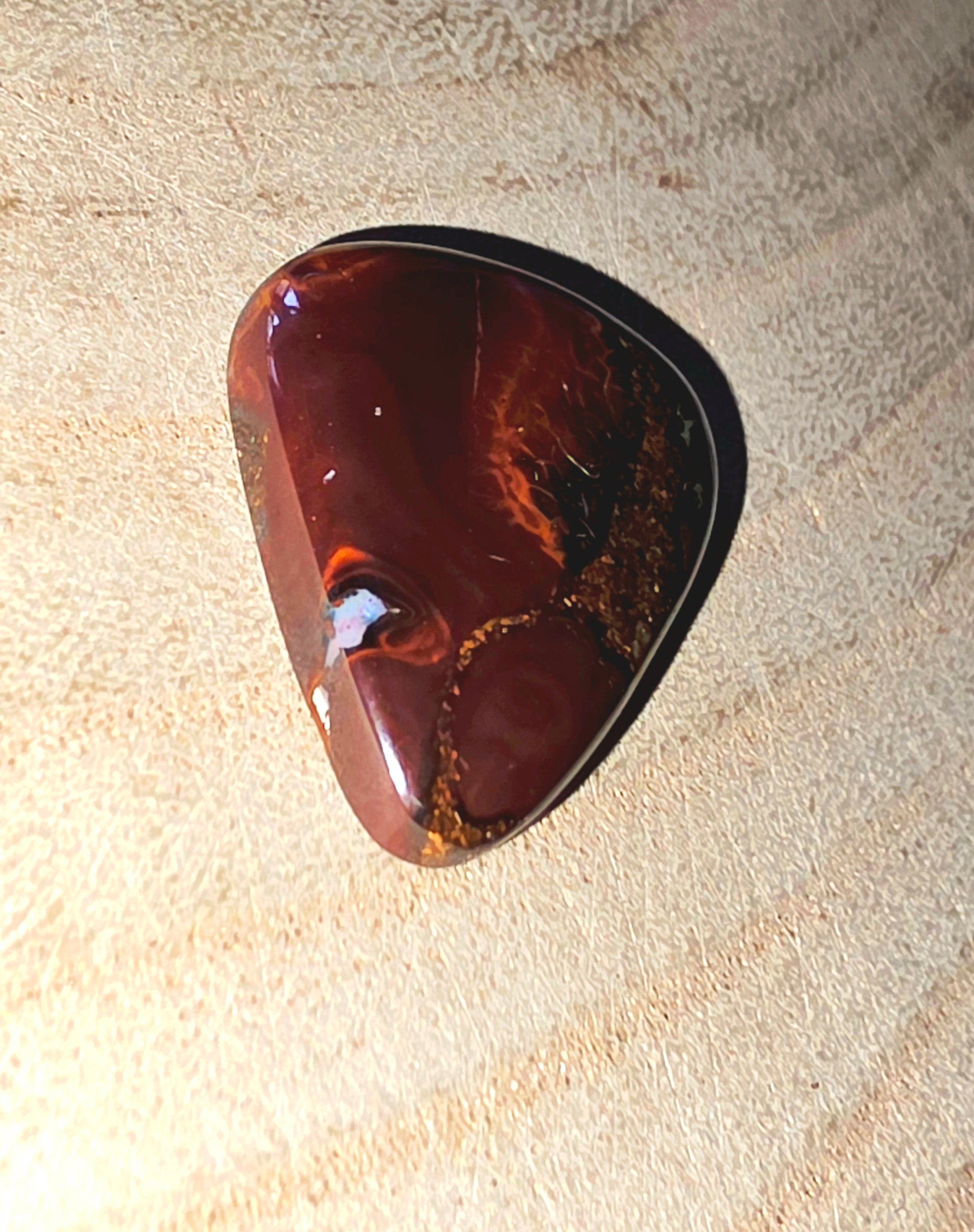Polished brown opal stone on a textured beige surface