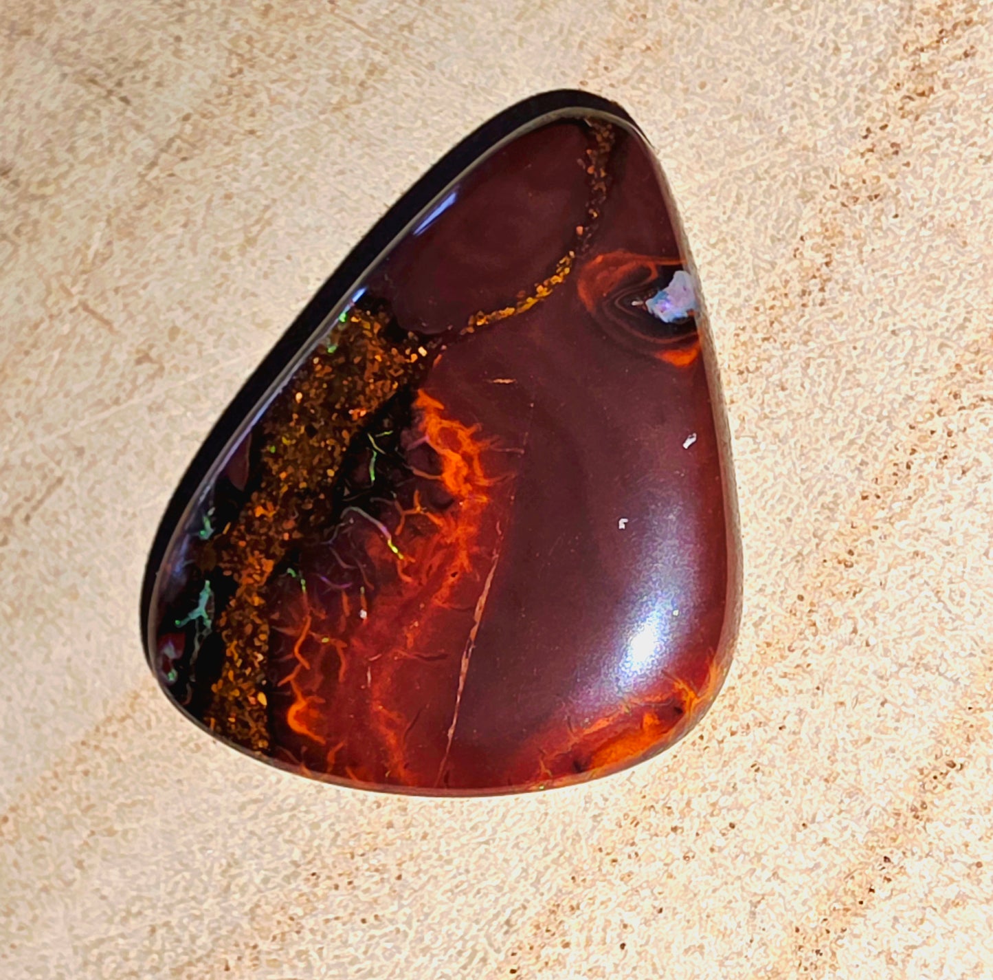Polished opal stone on a beige sandstone background