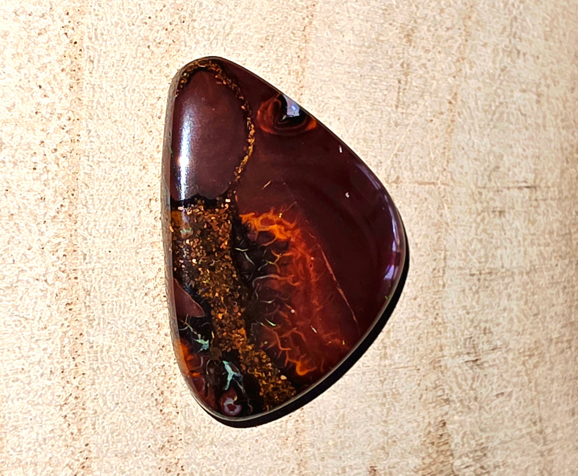 Polished brown and orange boulder opal on a beige textured background