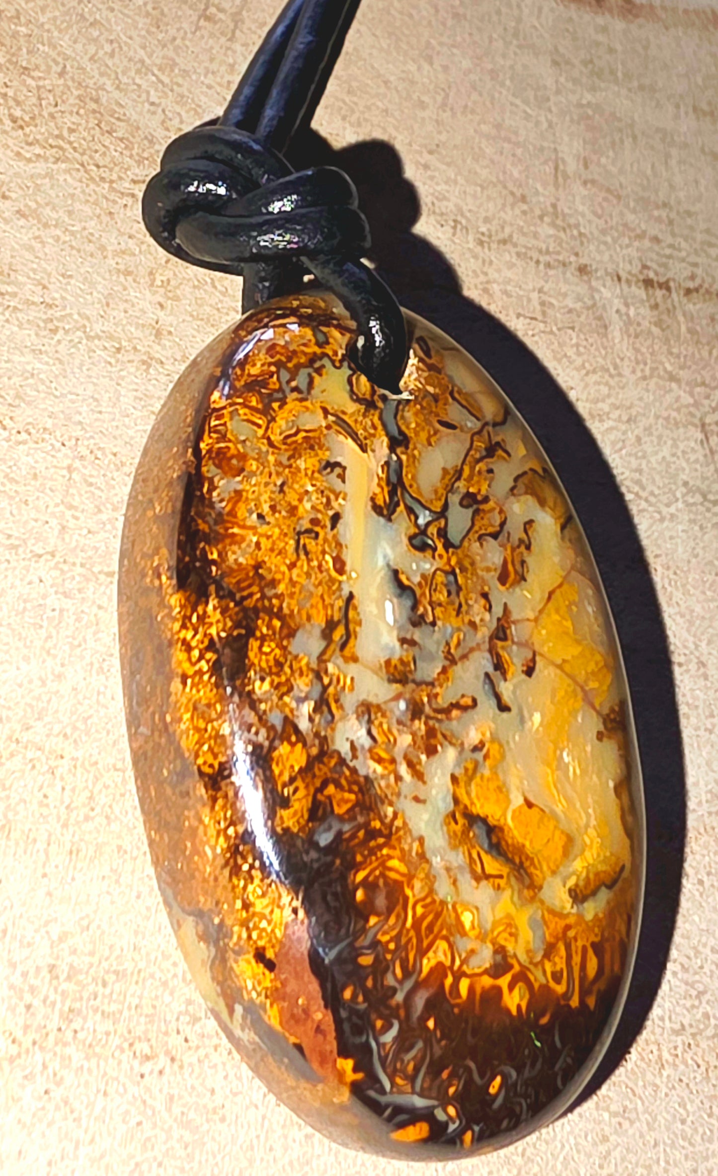 Oval-shaped opal pendant on a black cord against a beige background
