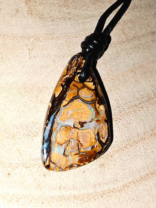 Tessellated boulder opal pendant on a black cord against a beige background