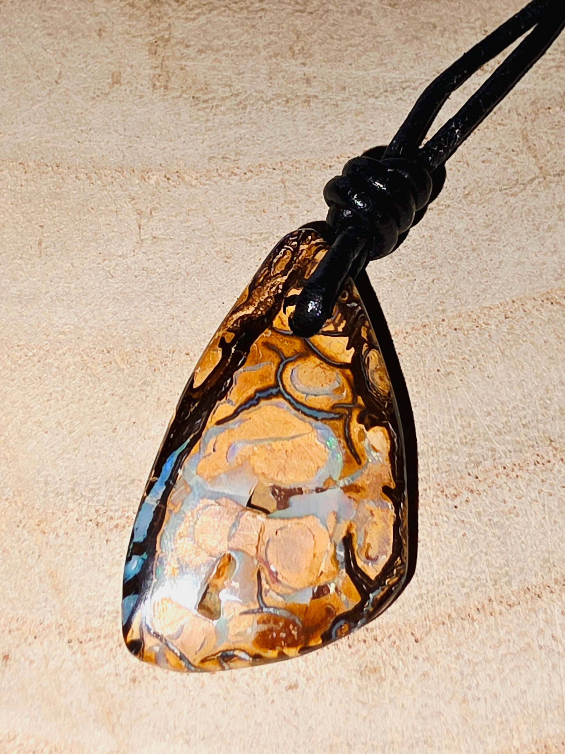 Teardrop-shaped opal pendant on a beige background