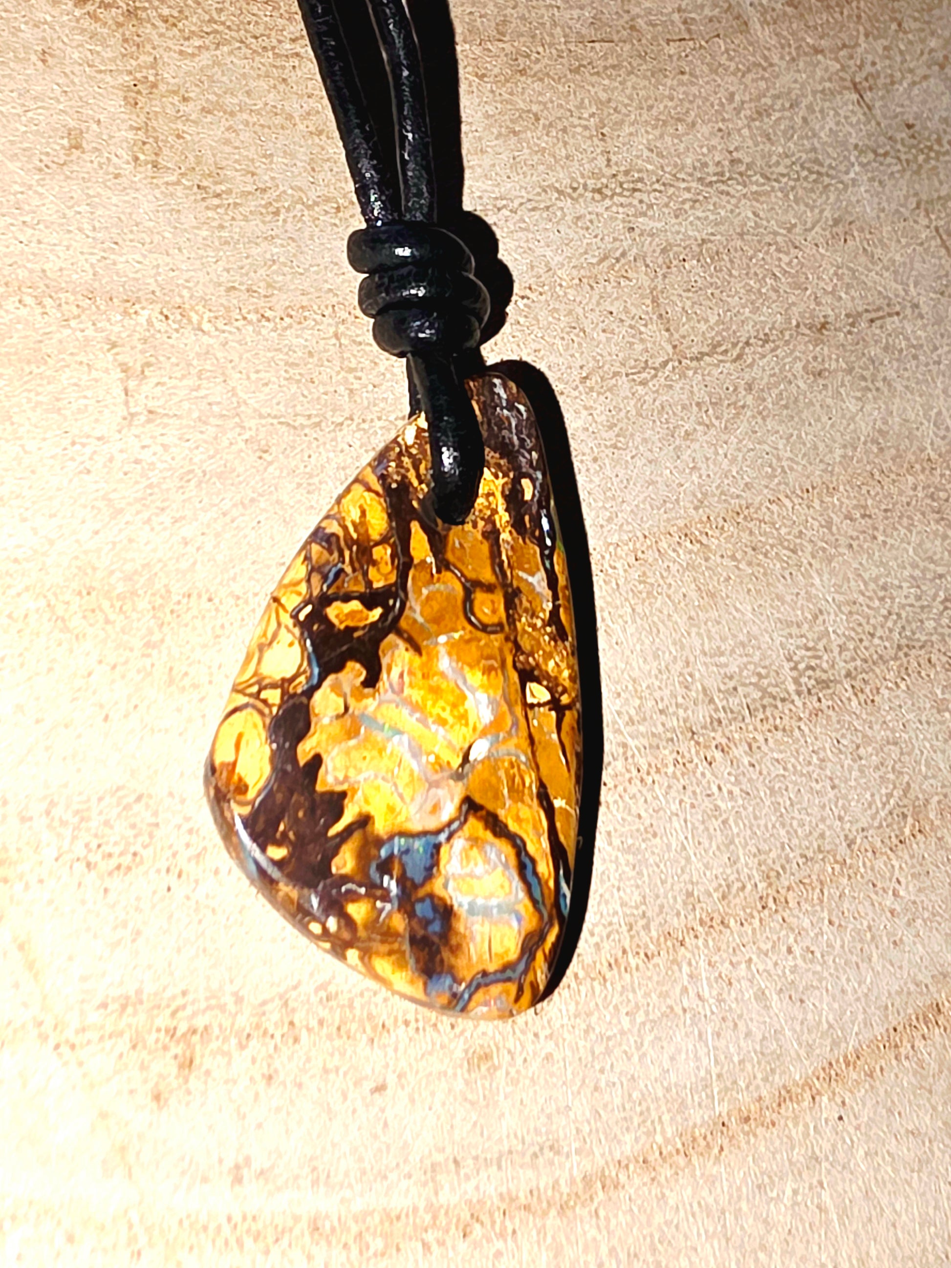 Teardrop-shaped opal pendant on a black cord against a beige background