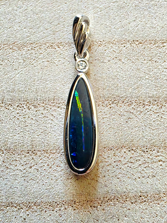 Teardrop-shaped opal pendant with silver frame on textured beige surface