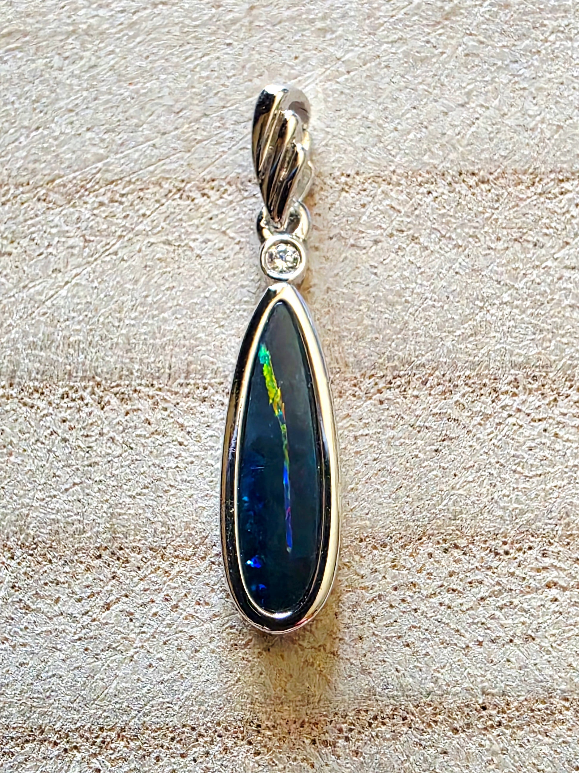 Teardrop-shaped pendant with a blue stone and silver setting on a textured beige surface