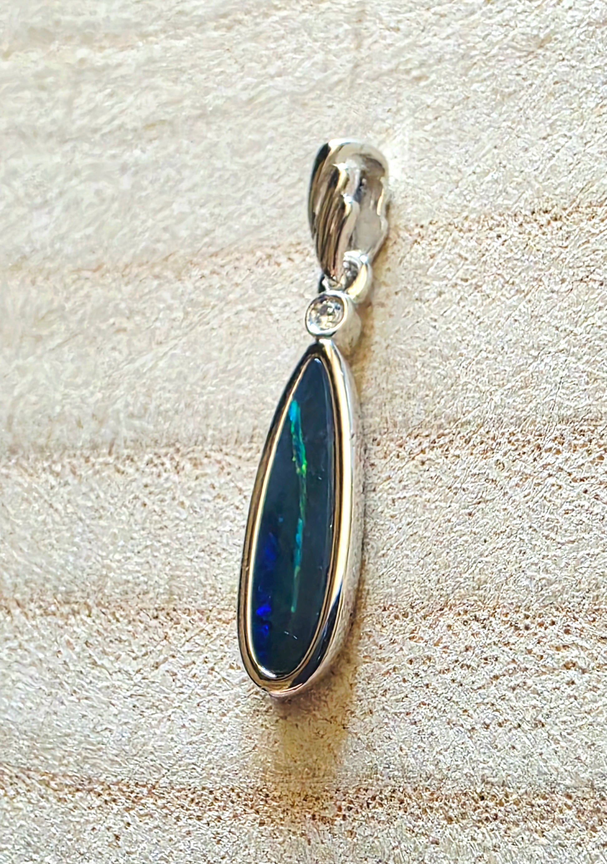 Opal pendant with silver setting on a textured beige surface