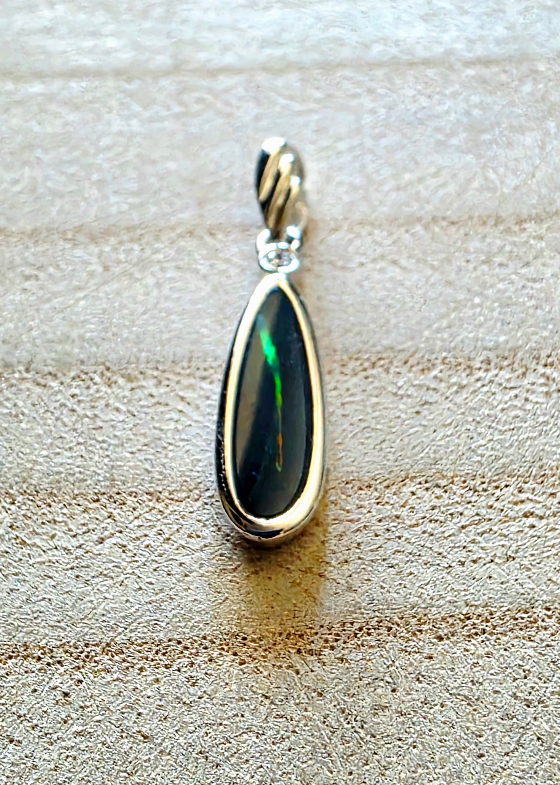 Teardrop-shaped pendant with silver frame on a textured beige surface