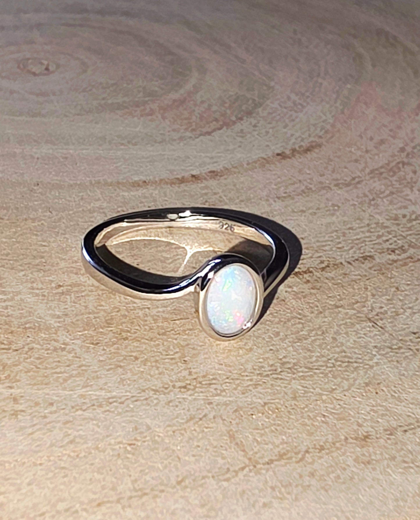 Silver ring with an opal stone on a wooden surface