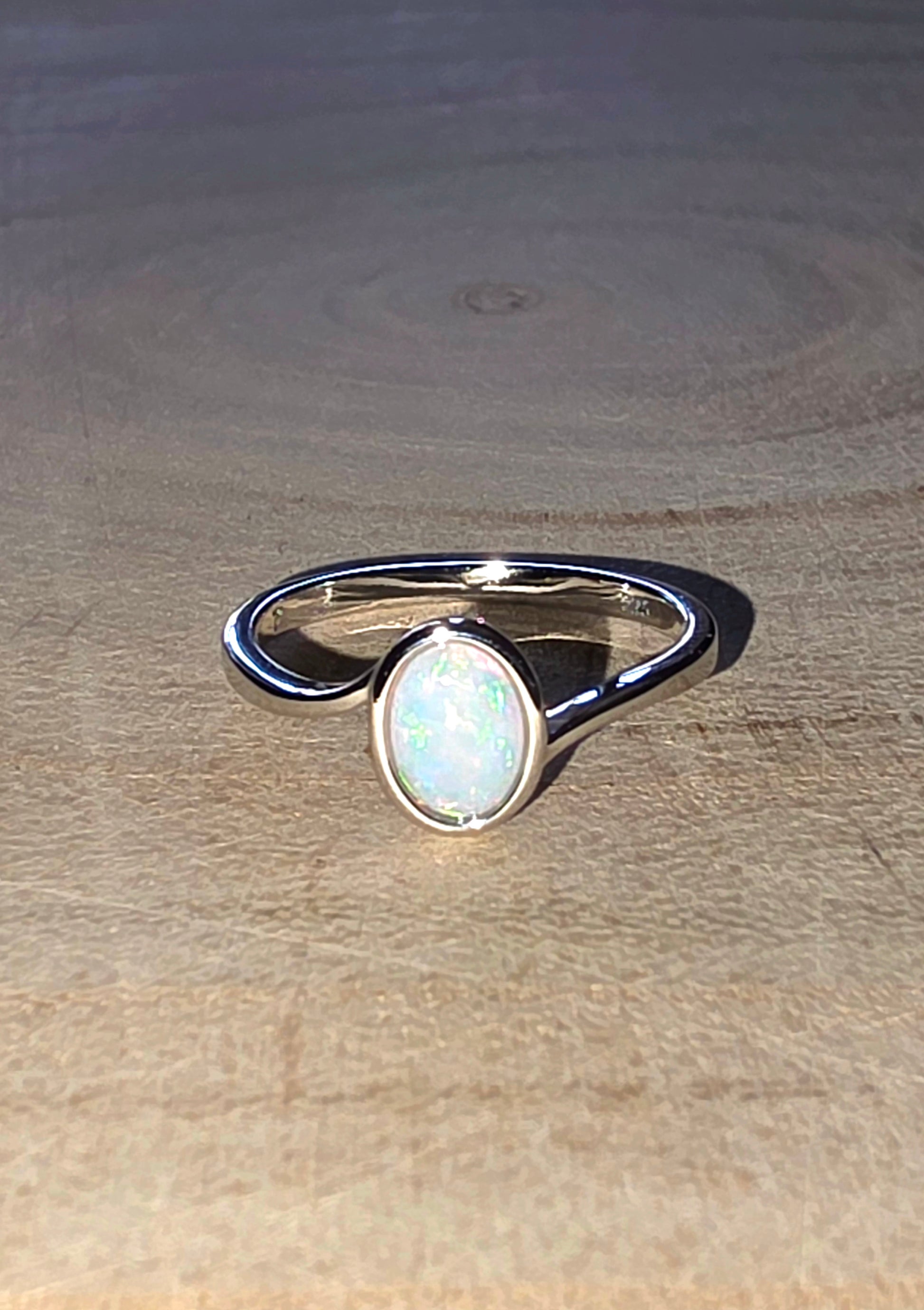 Silver ring with a white opal stone on a wooden surface