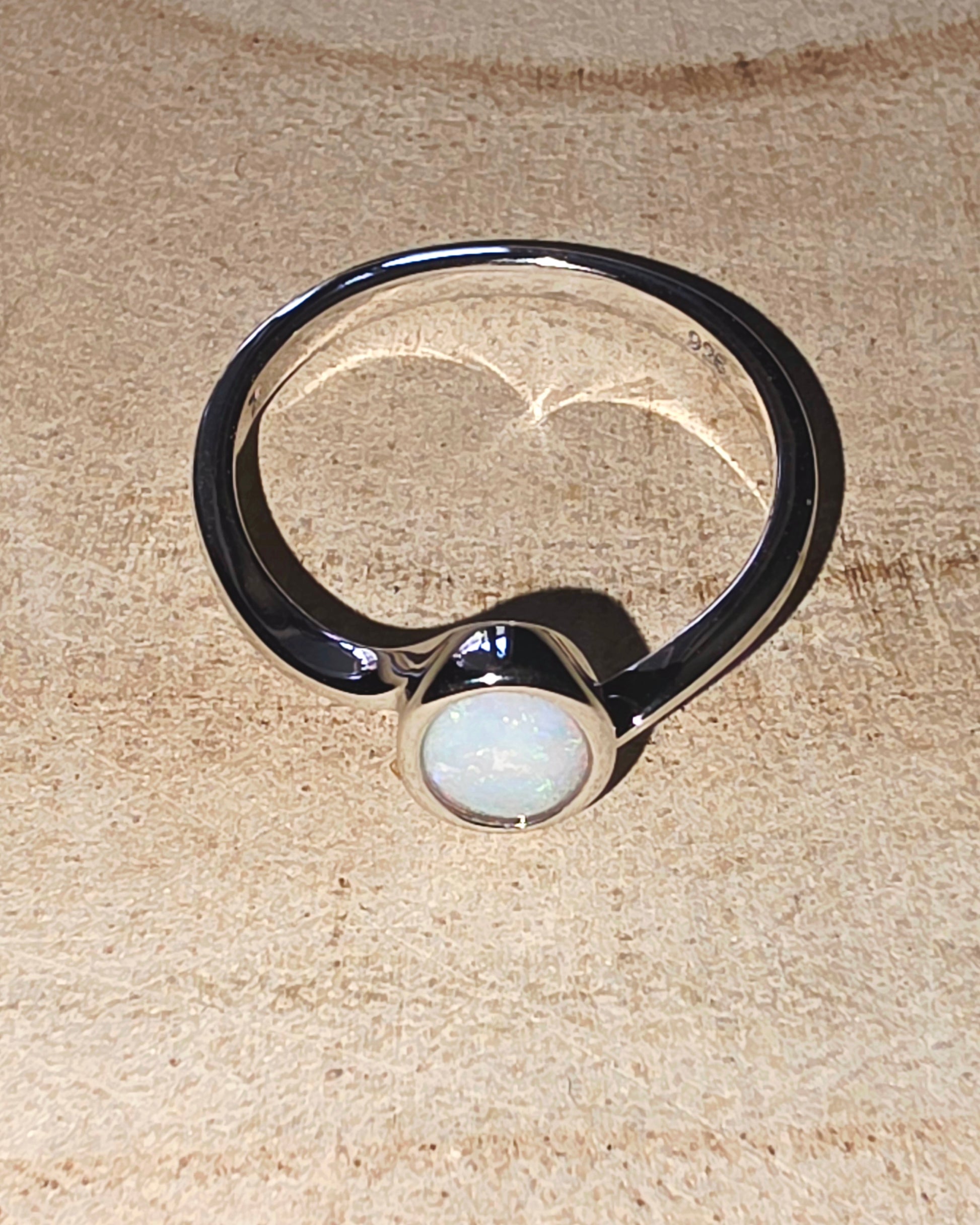 Silver ring with a central opal on a textured beige surface