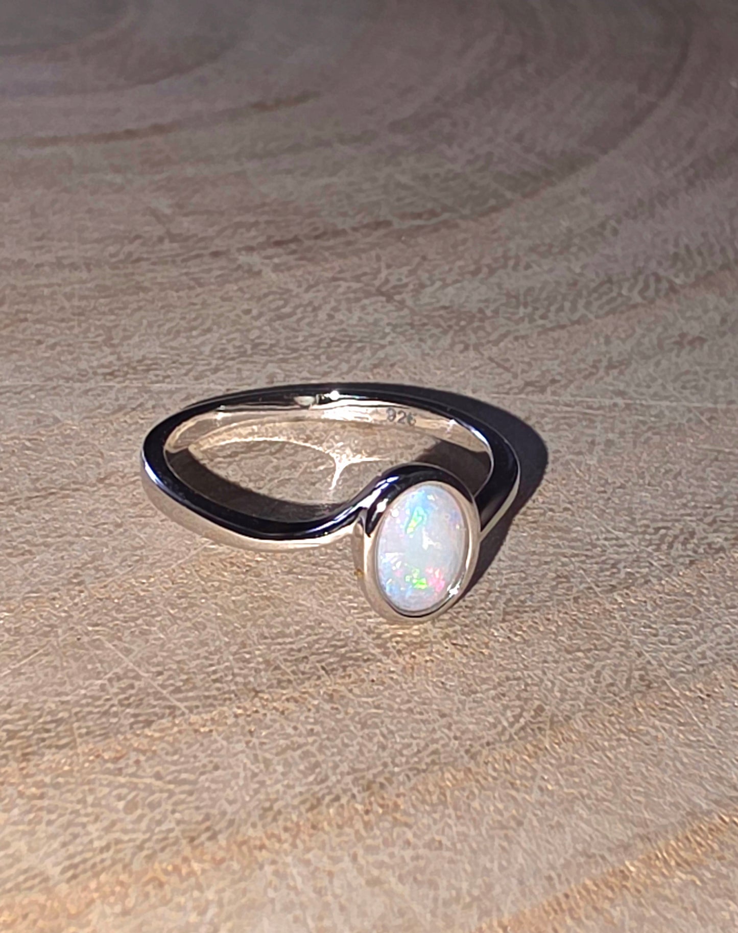Silver ring with a white opal stone on a textured beige surface