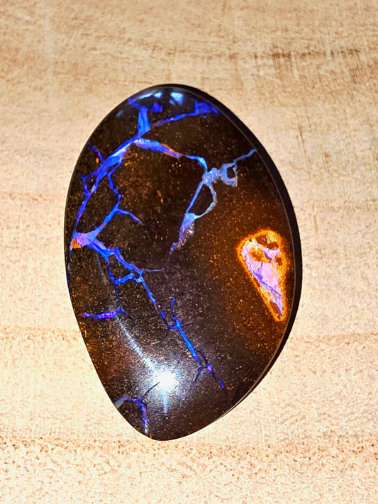 Polished opal gemstone with blue and orange fractures on a beige background