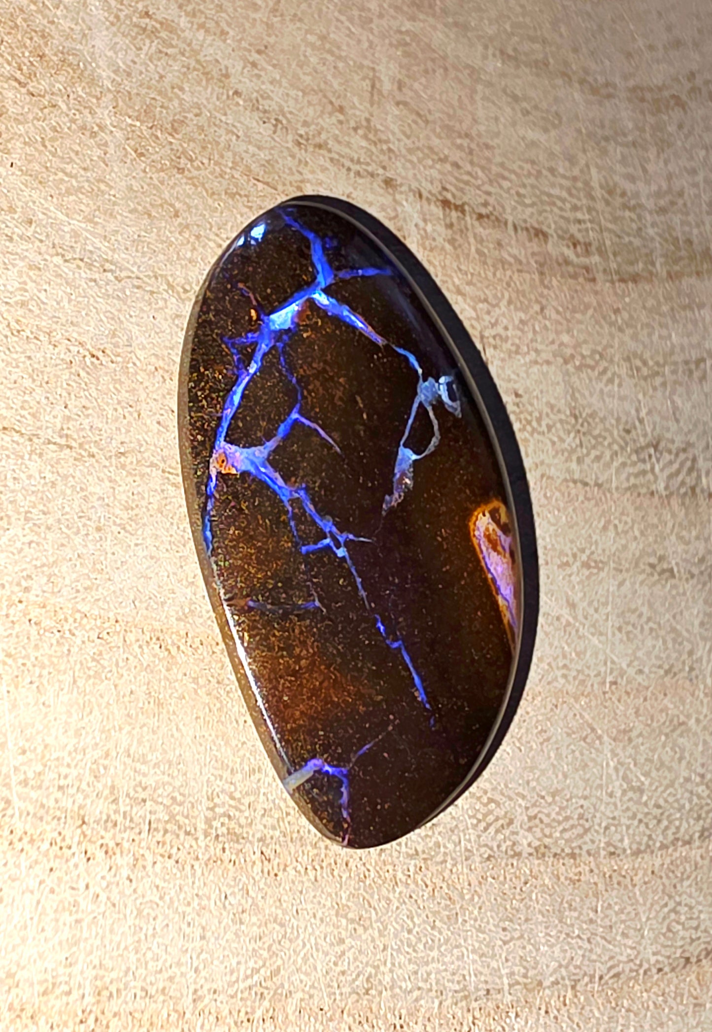 Polished boulder opal stone with blue and purple fractures on a beige background