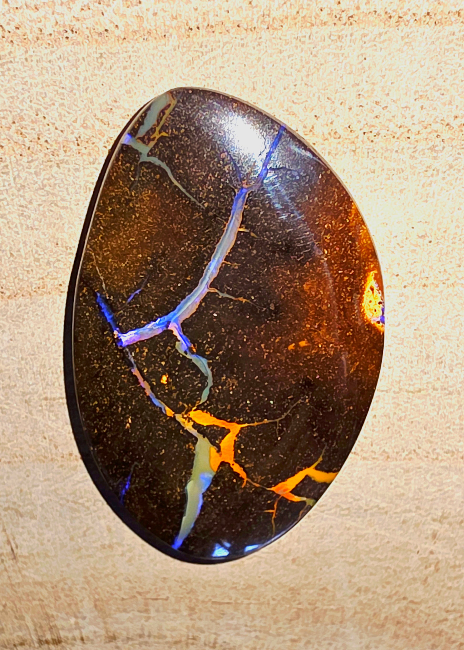 Polished gemstone with colourful inclusions on a beige background