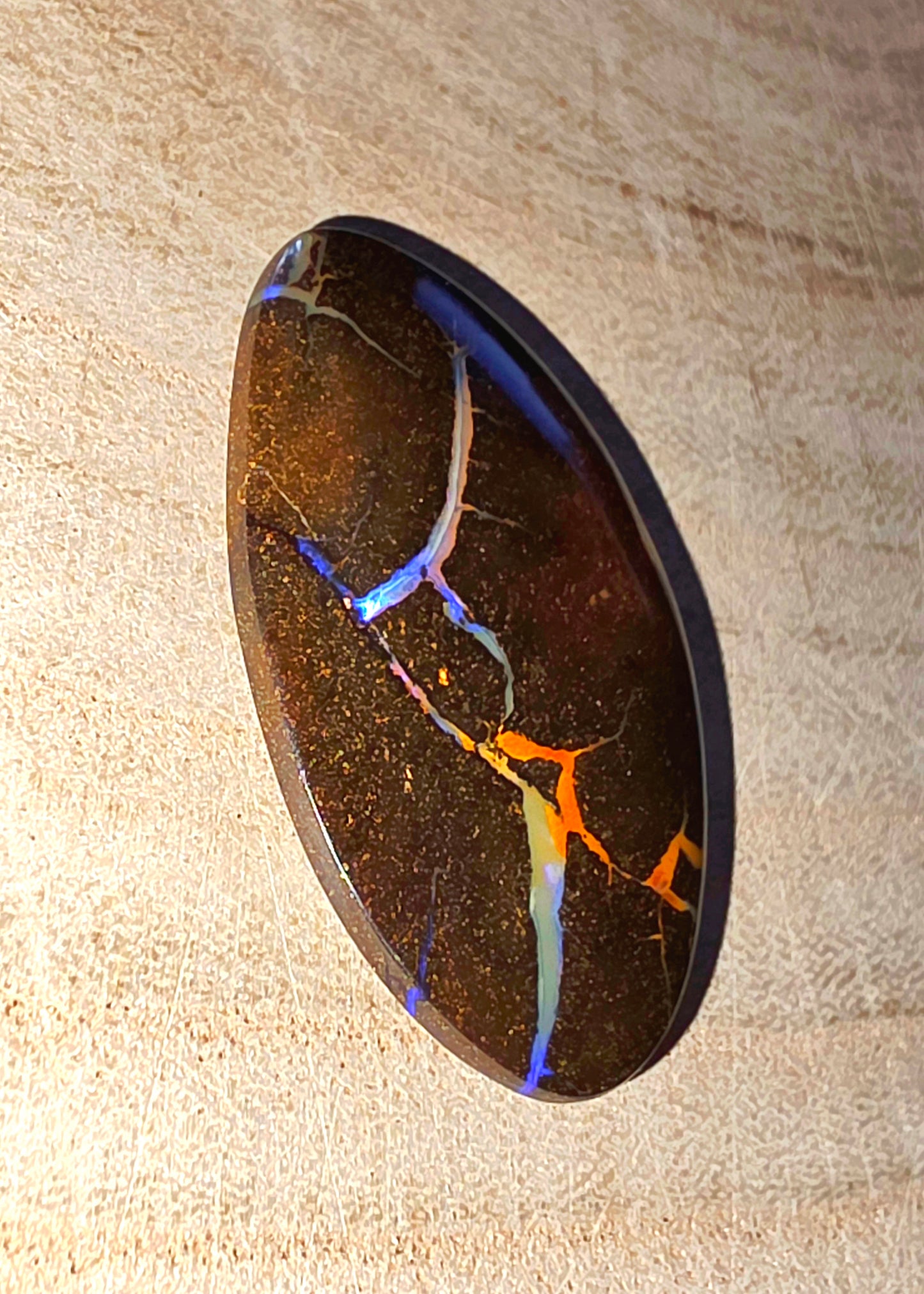 Polished opal stone with colourful inclusions on a beige background