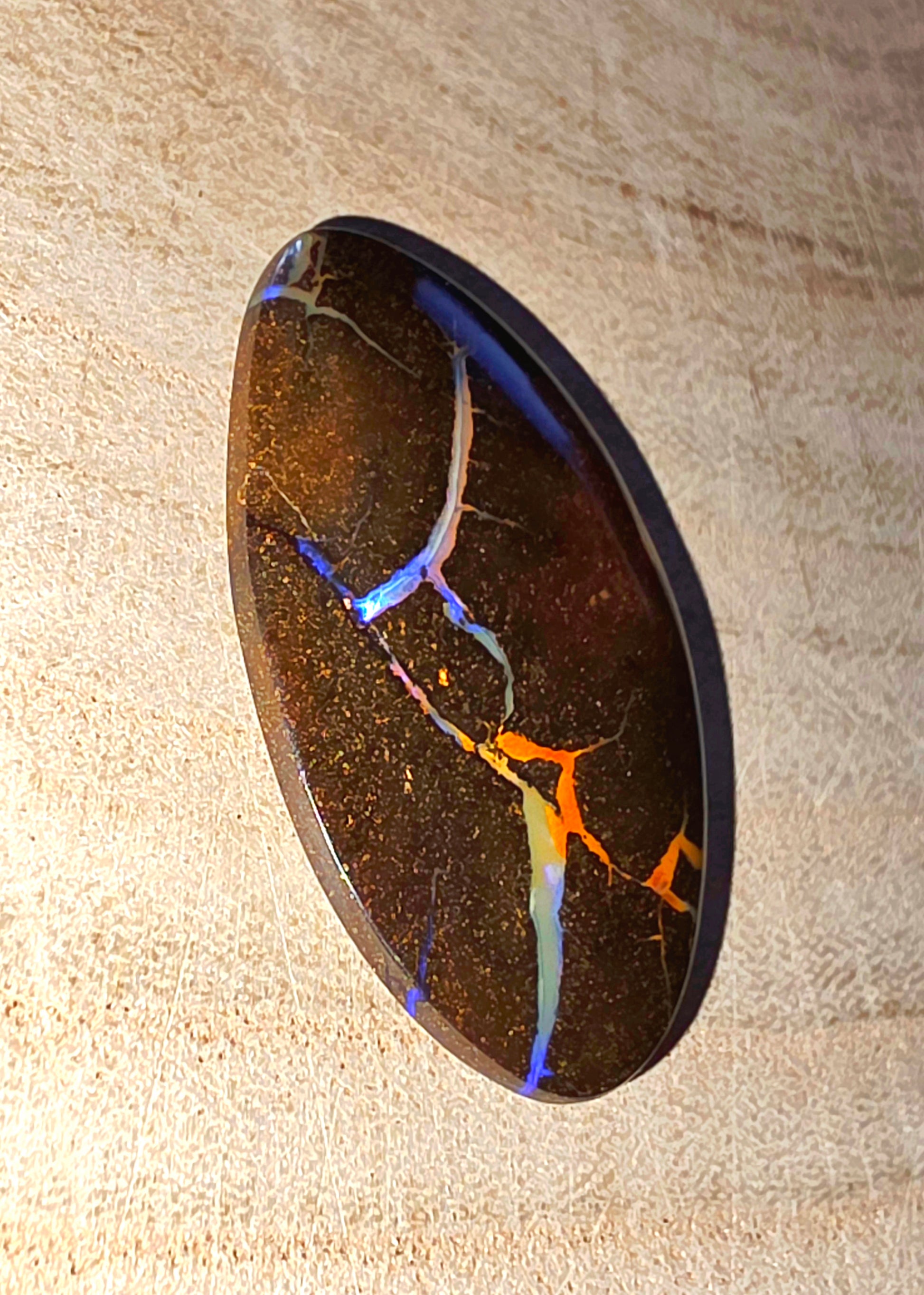 Polished opal stone with colourful inclusions on a beige background