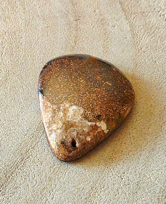 Brown boulder opal stone on a beige textured surface