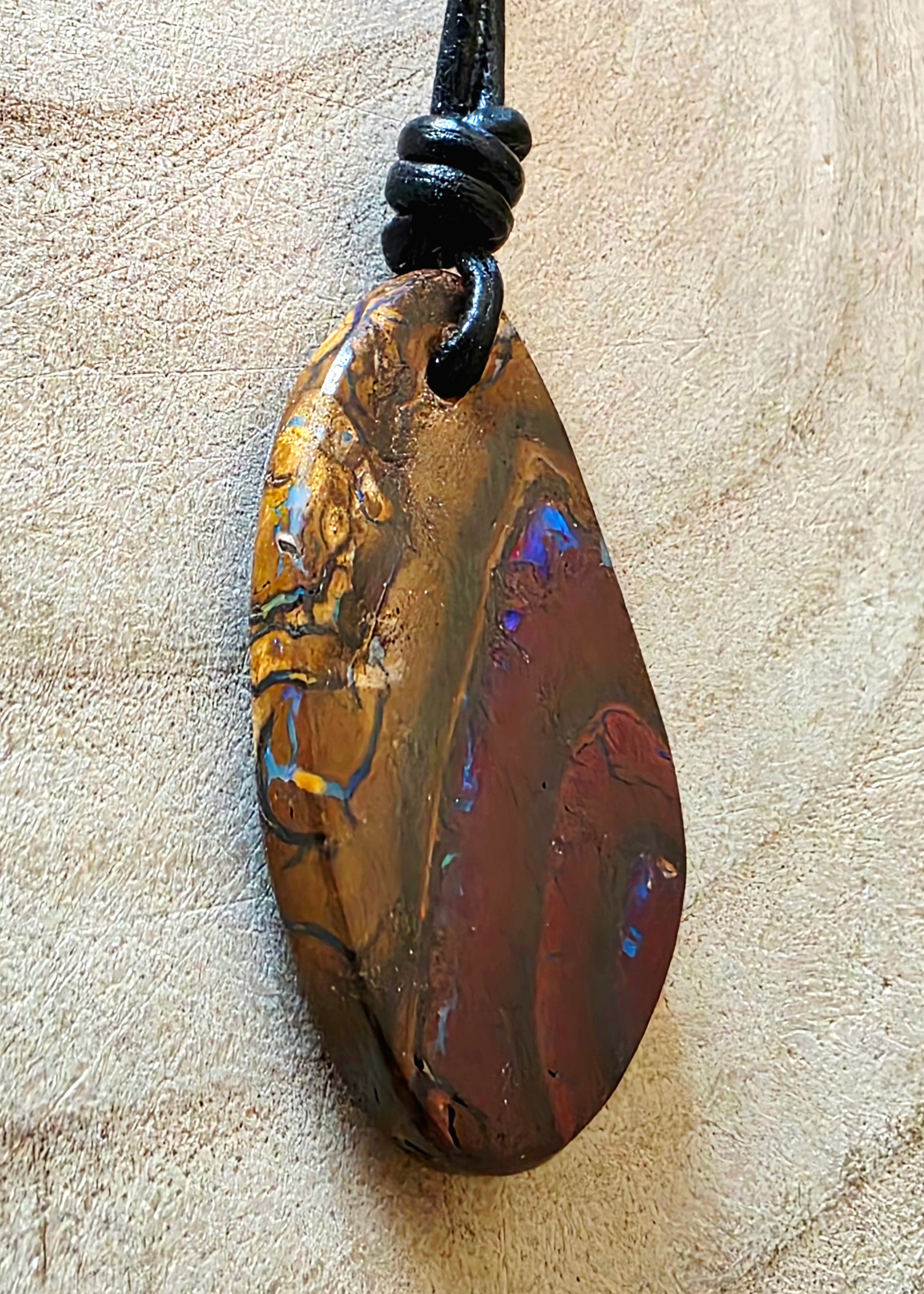 Boulder opal pendant on a black cord against a beige background