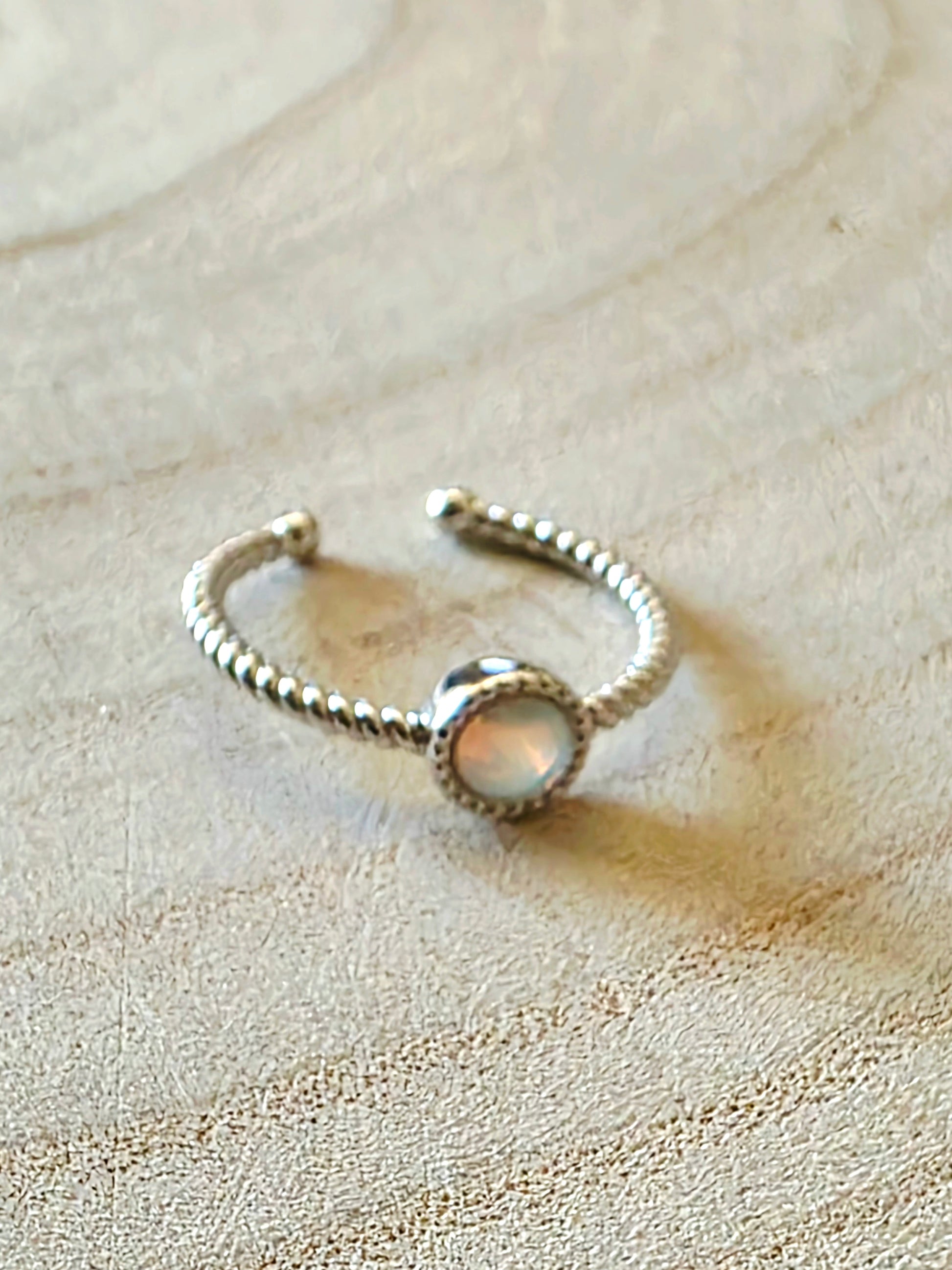 Silver ring with an opal on a textured beige surface